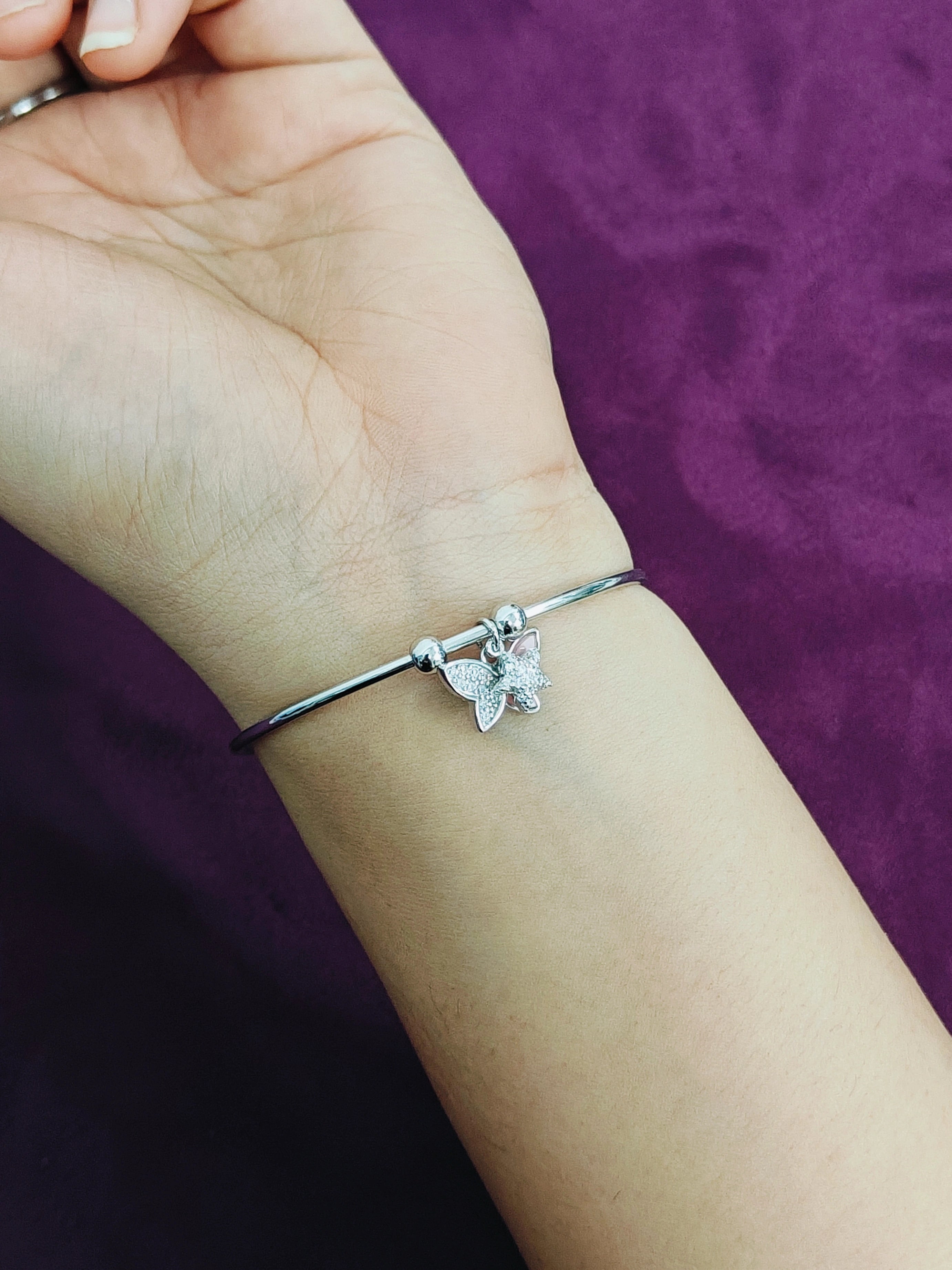 Silver bracelet with a butterfly charm on a wrist against a purple background