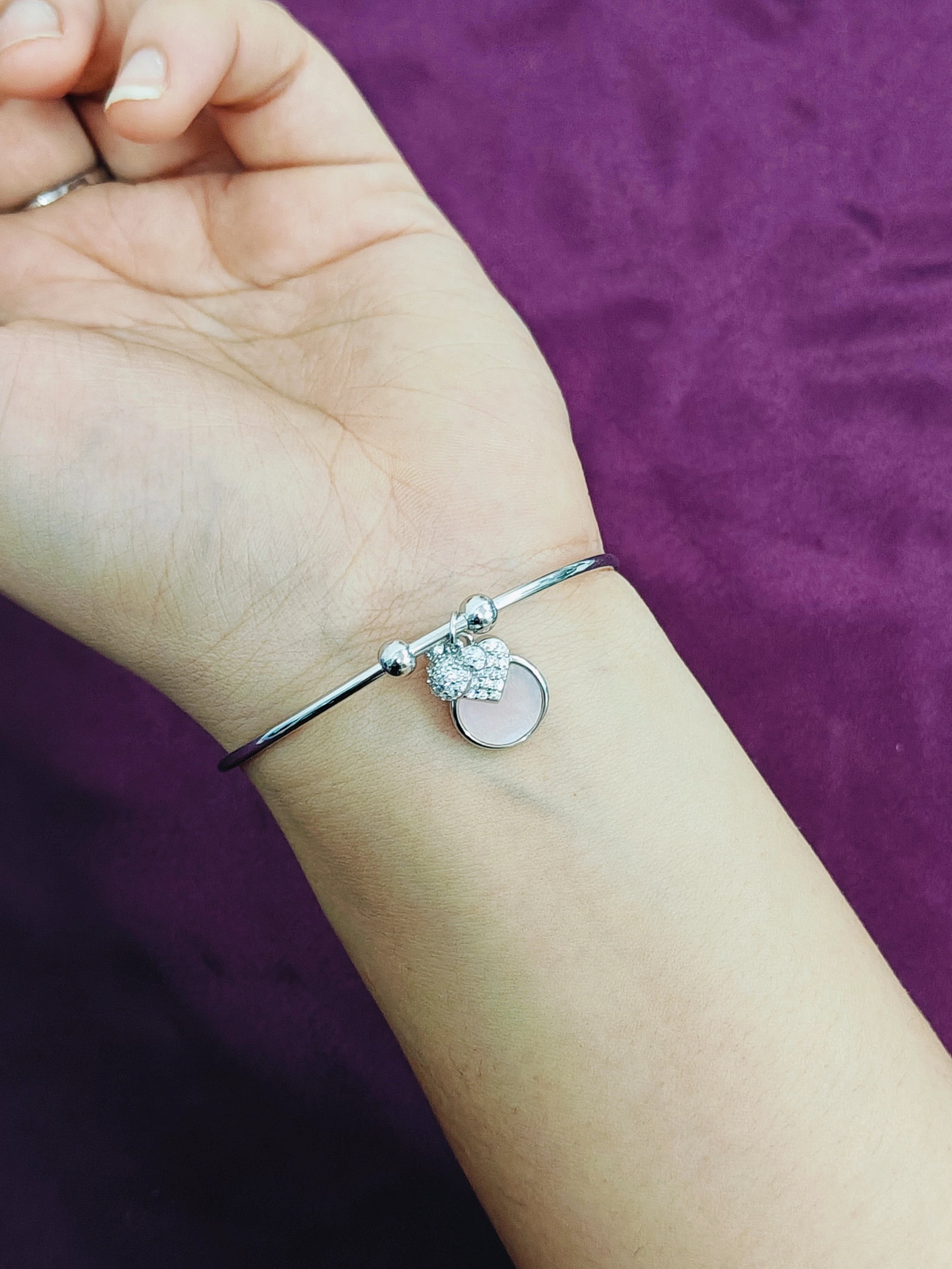 Silver bracelet with heart charm on a wrist against a purple background
