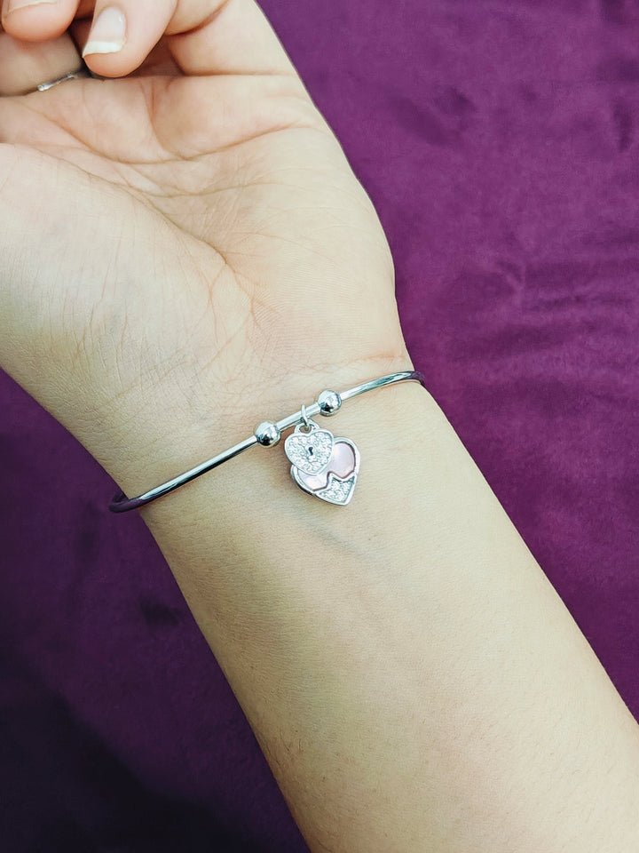 Silver bracelet with a heart charm on a wrist against a purple background