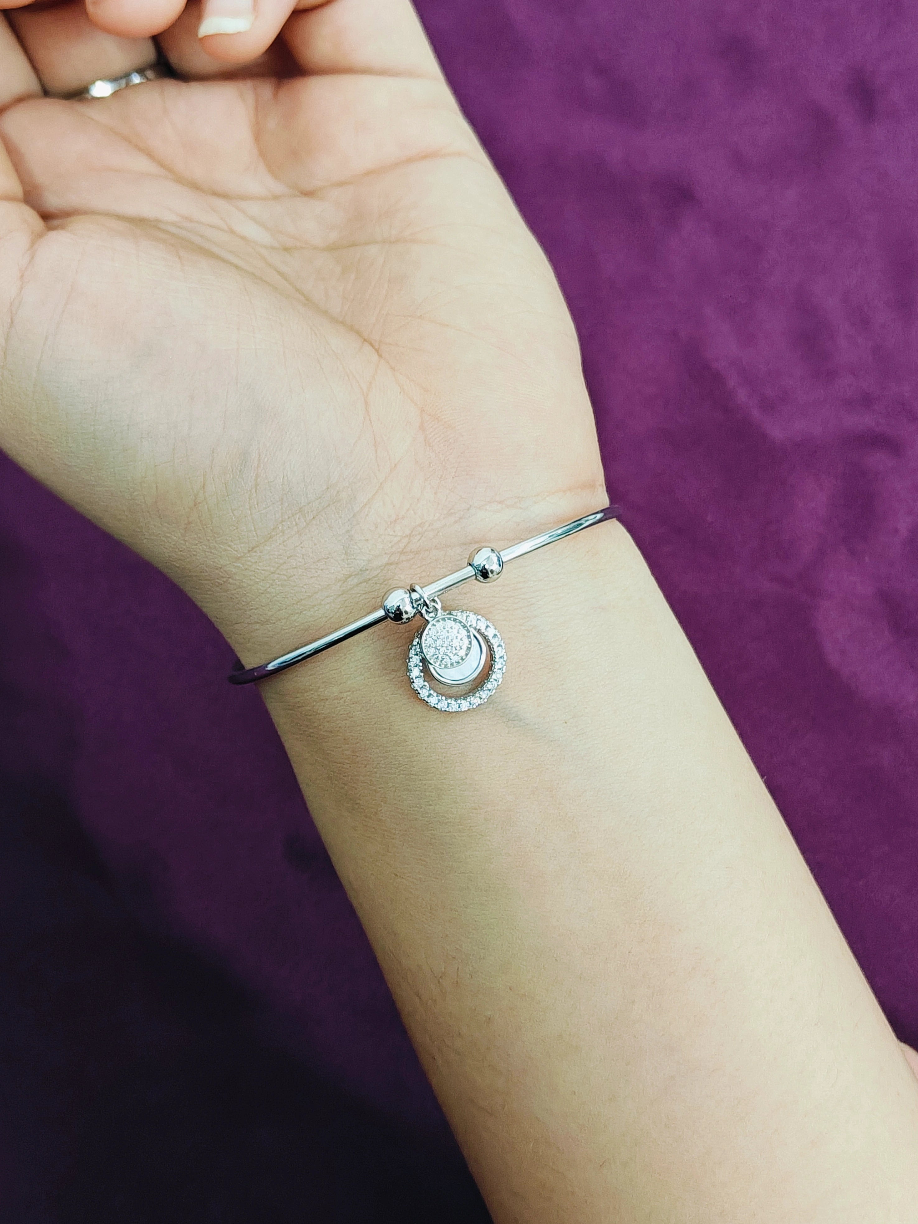 Silver bracelet with a round charm on a wrist against a purple background