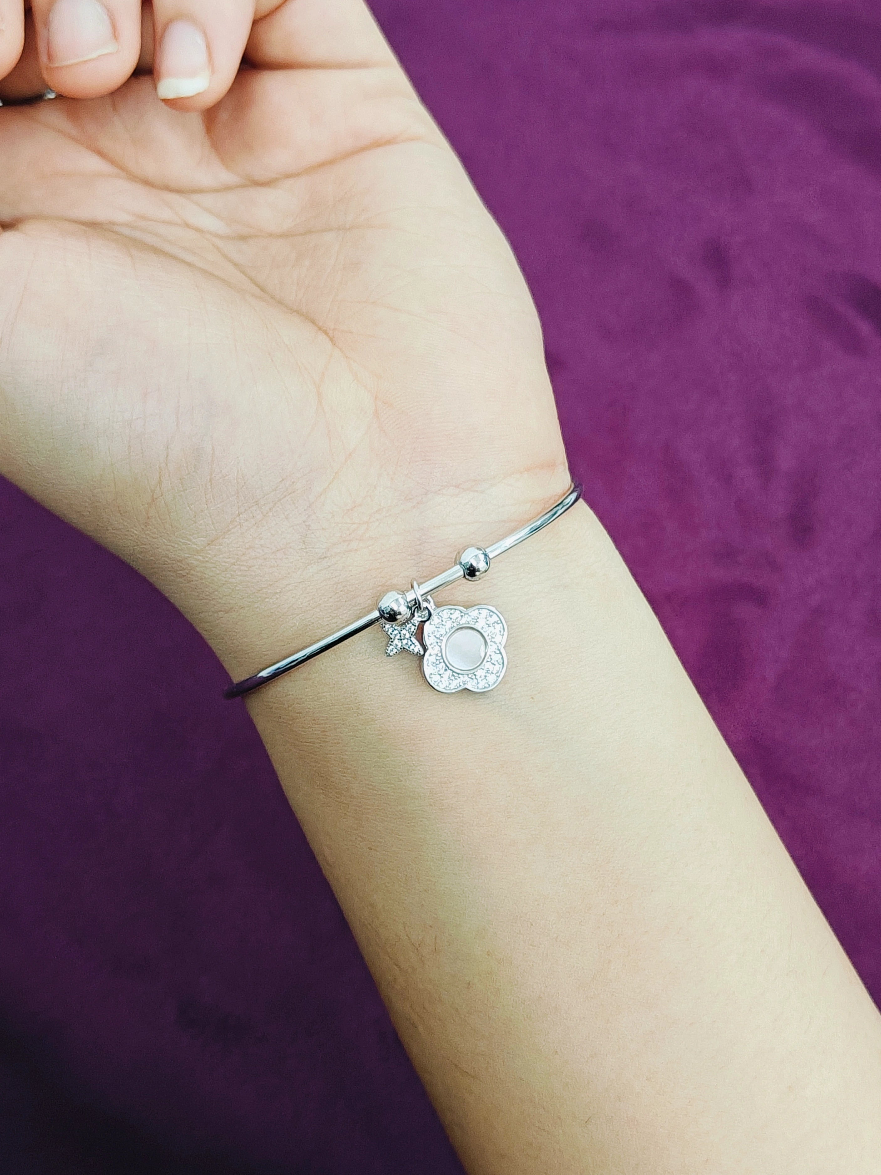 Silver bracelet with charms on a wrist against a purple background