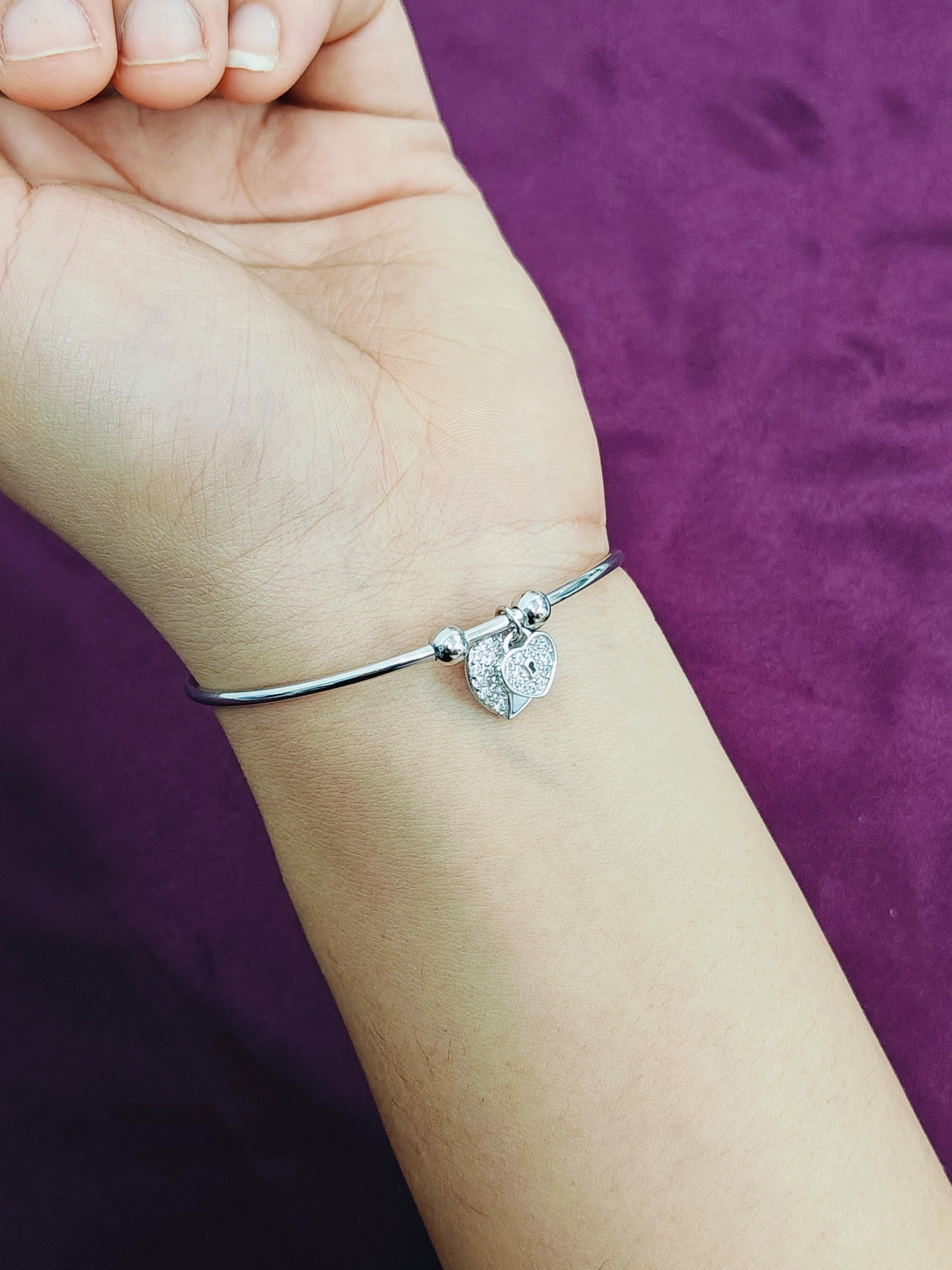 Silver bracelet with a heart charm on a wrist against a purple background