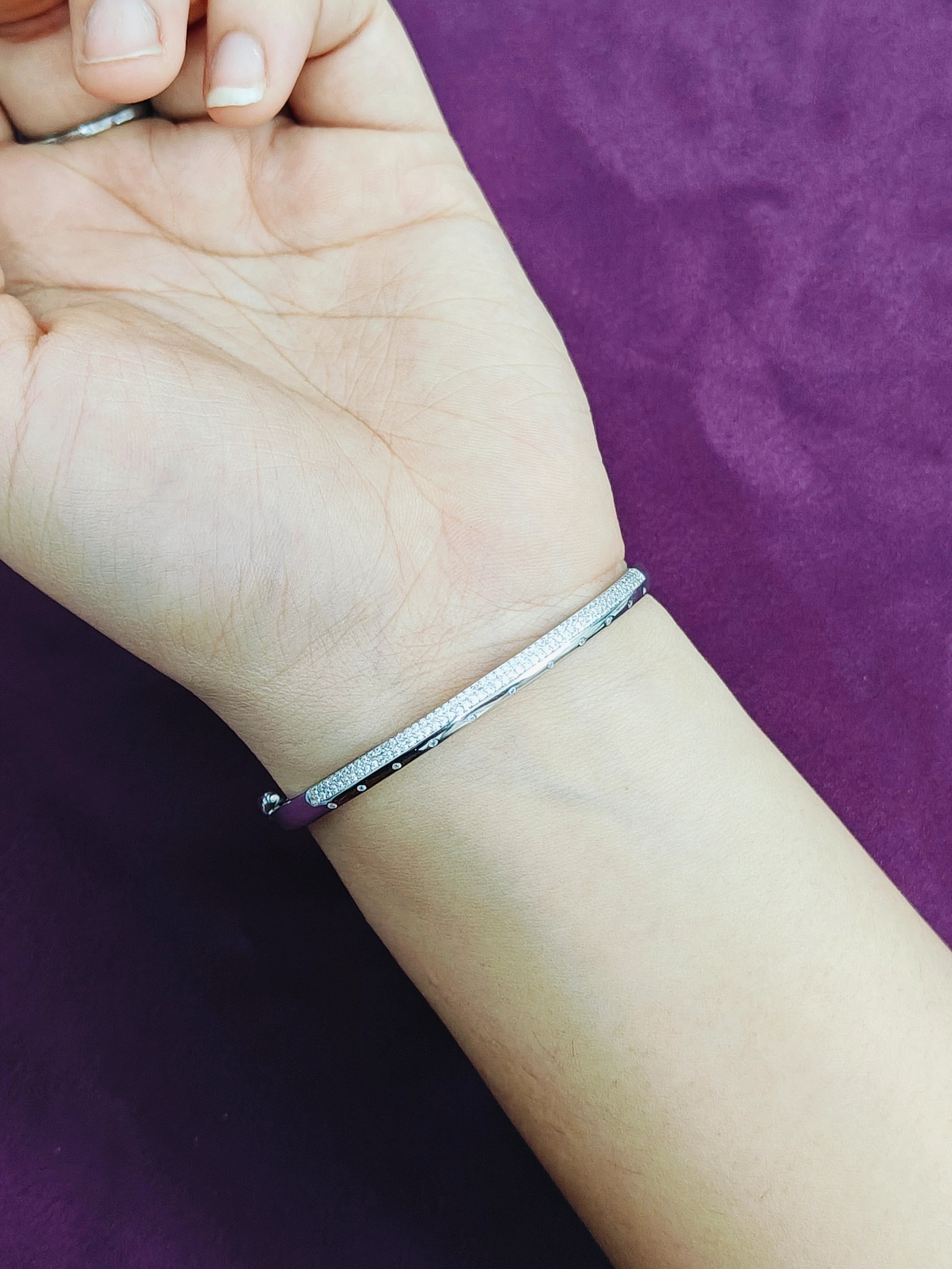 Silver bracelet on a wrist with a purple background
