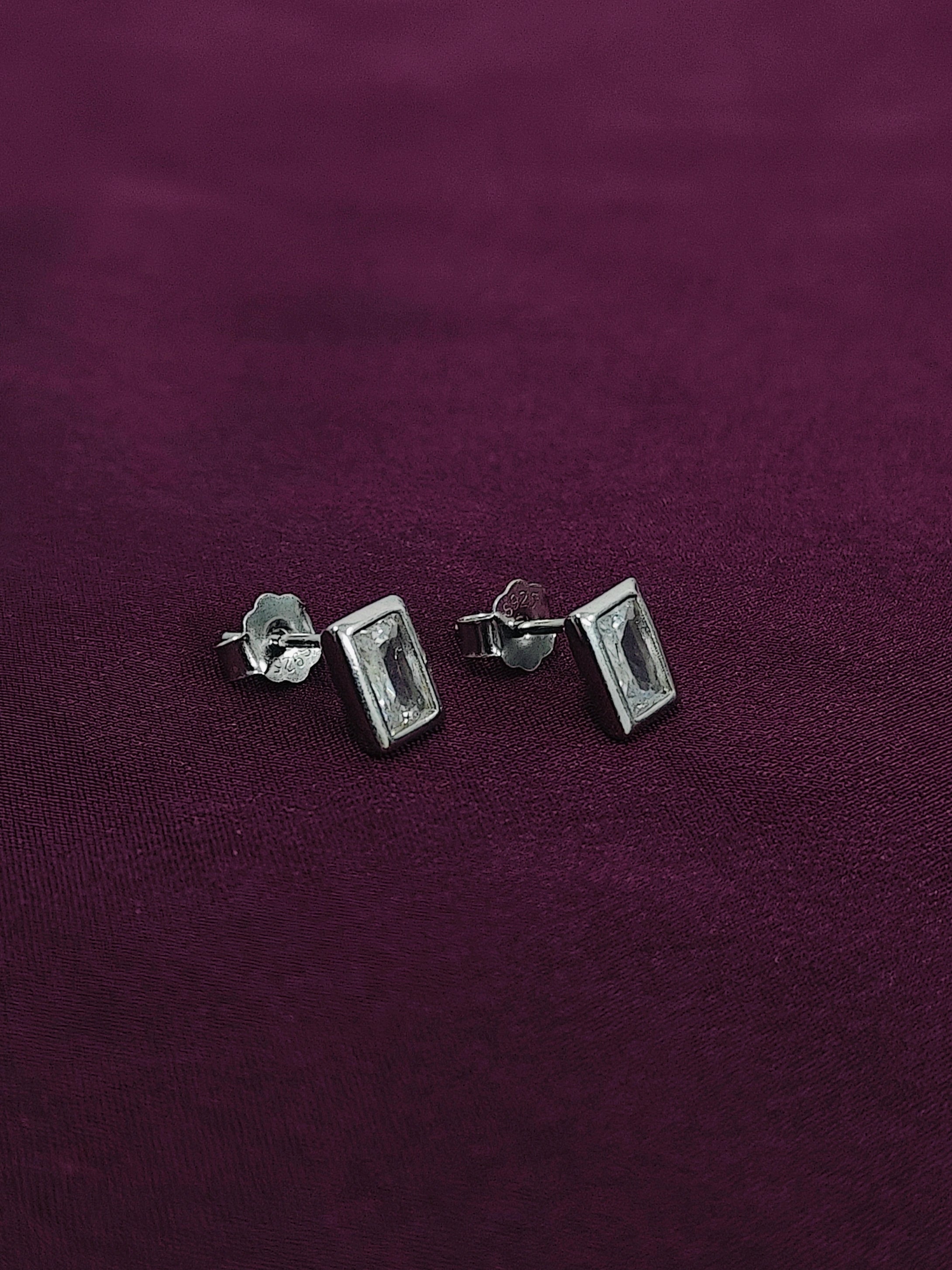 Silver rectangular stud earrings on a purple fabric background