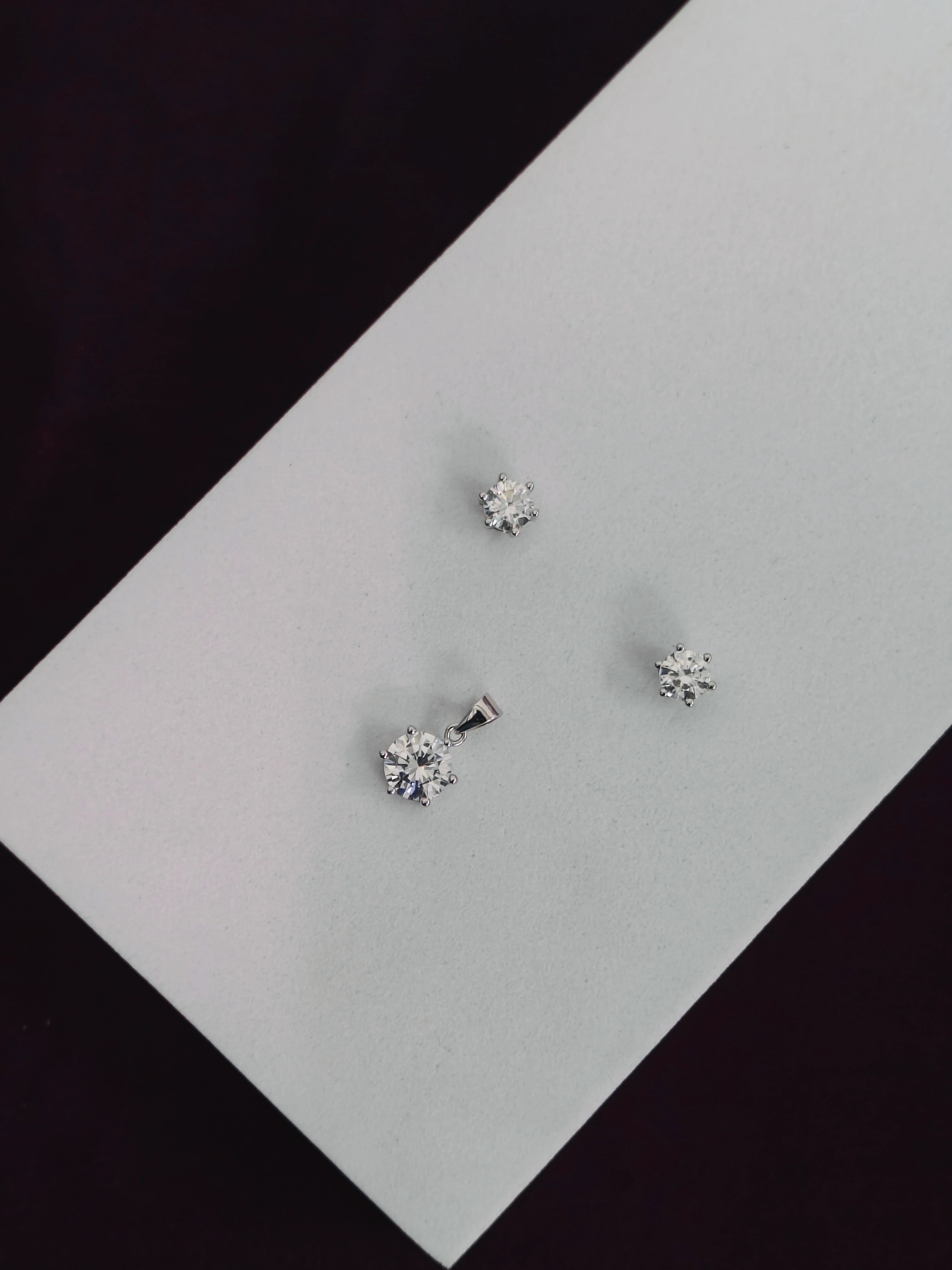 Three diamond stud earrings on a light gray surface with a black background
