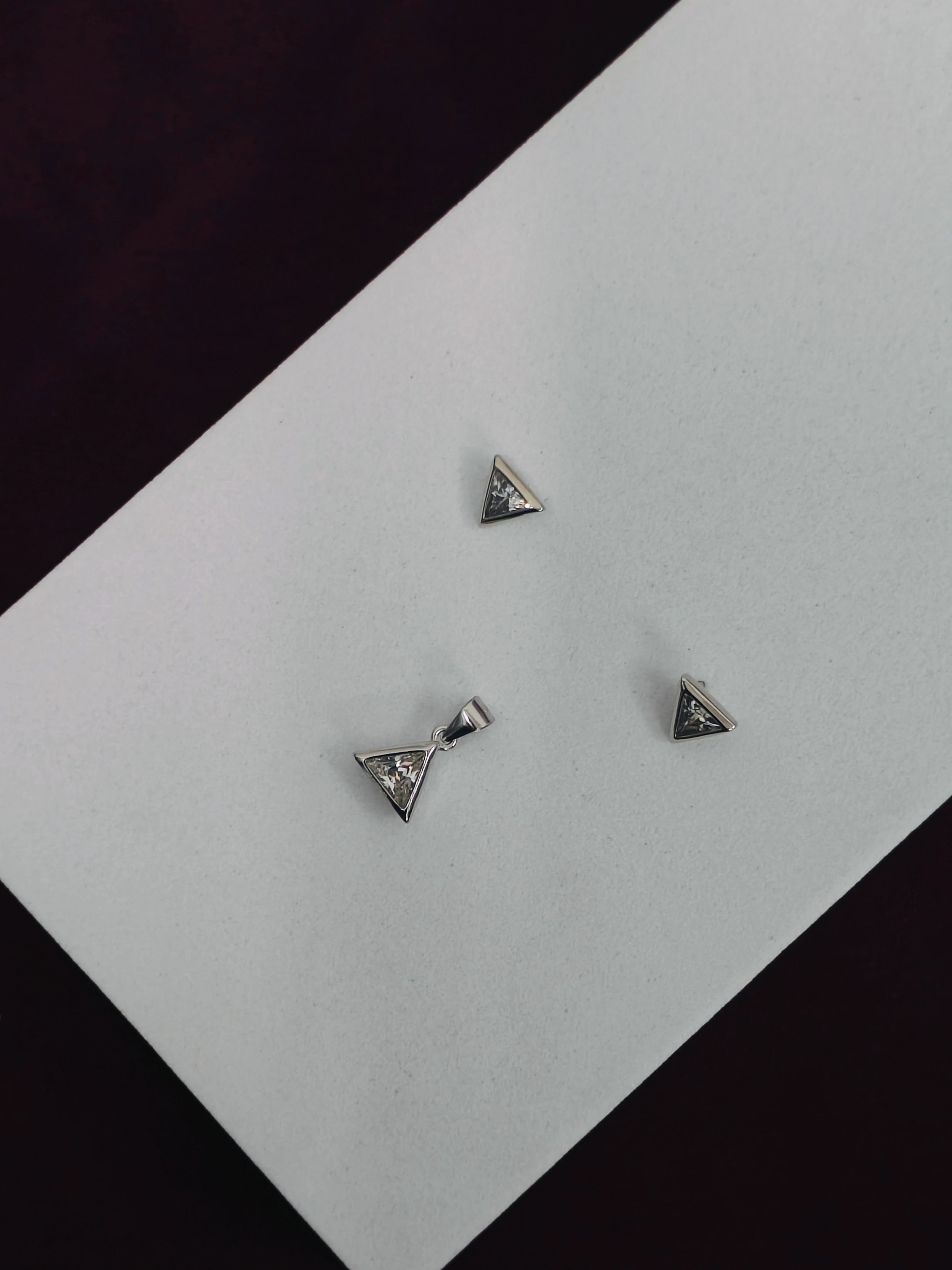 Three triangle-shaped earrings on a light gray surface with a black background