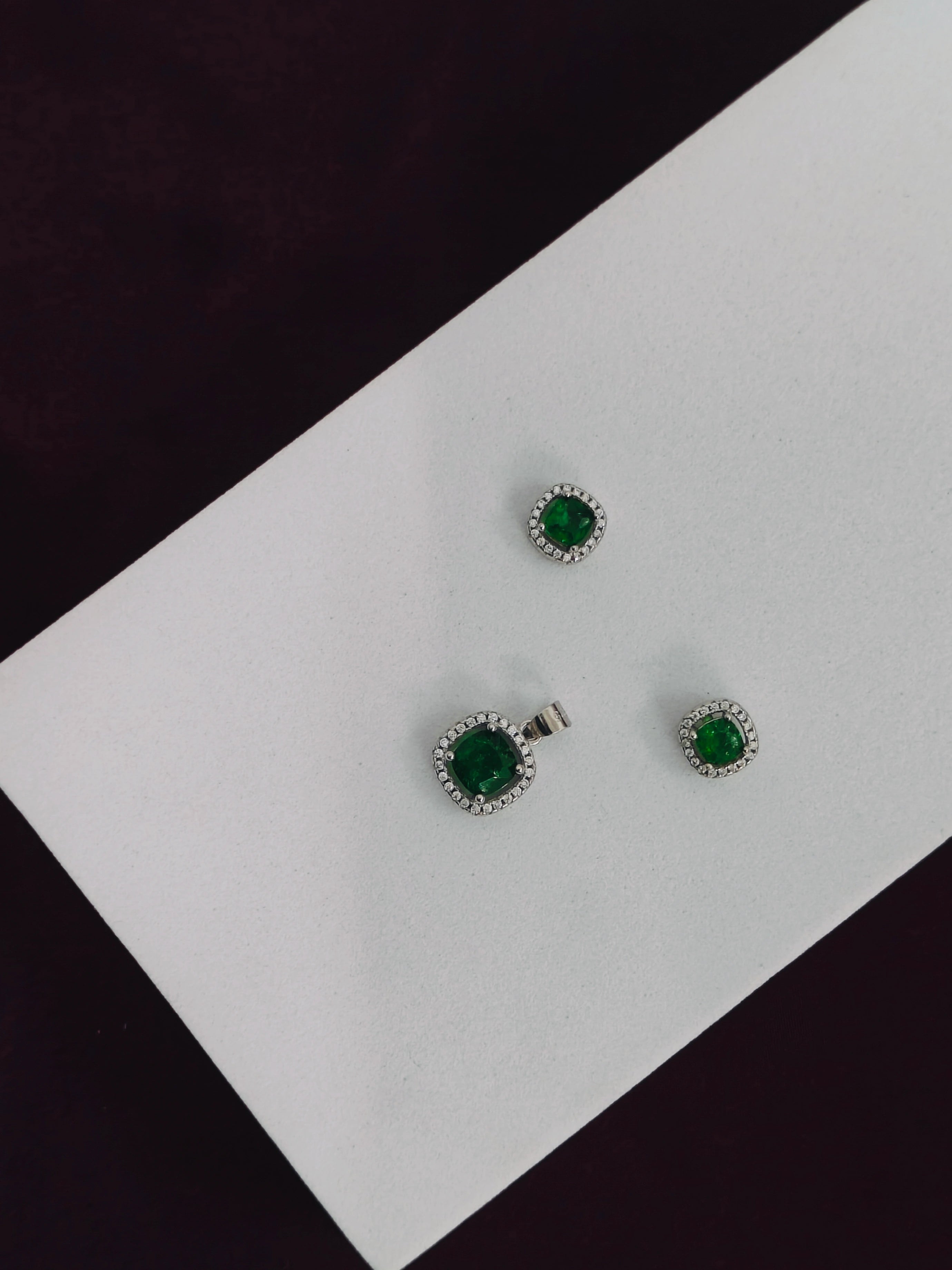 Pair of emerald green gemstone earrings on a white card with a black background