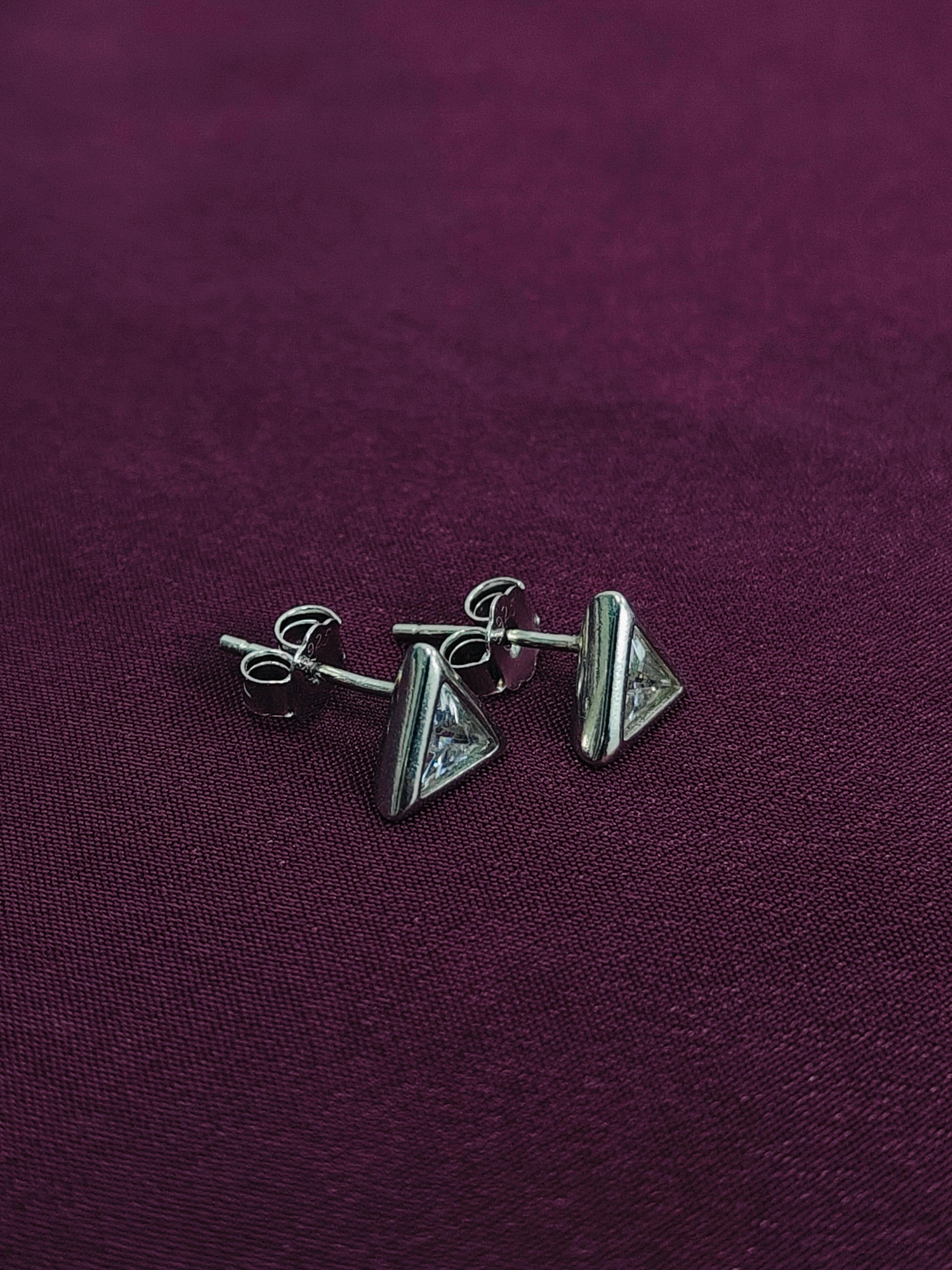 Pair of silver triangle earrings on a purple fabric background