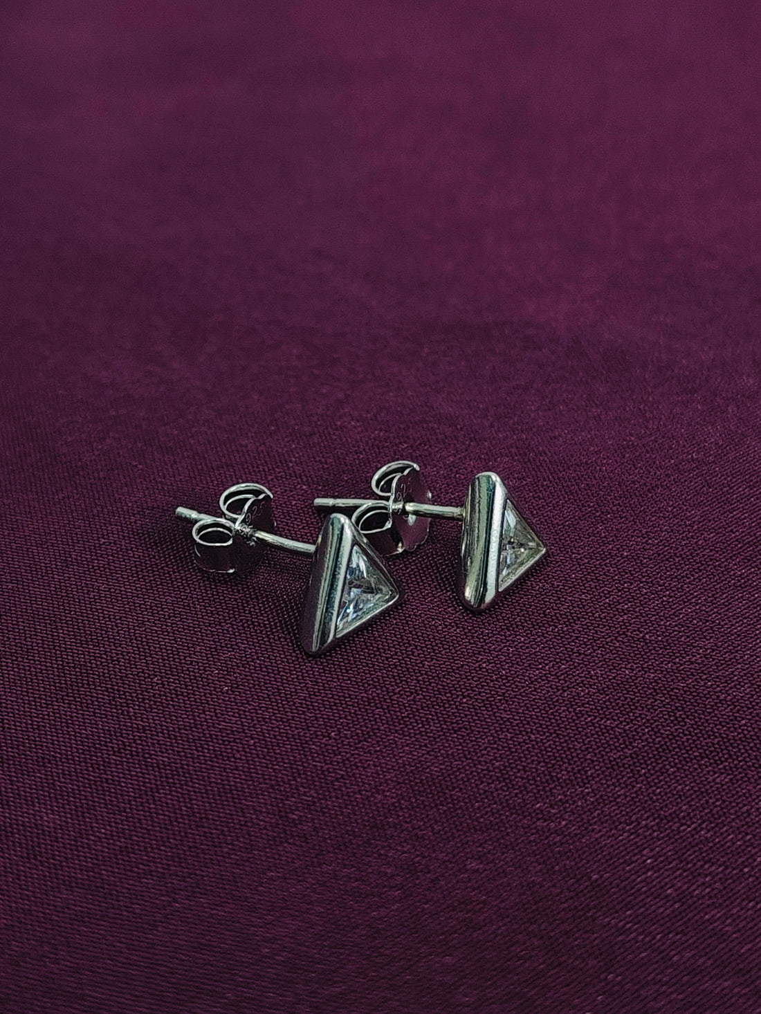 Pair of silver triangle earrings on a purple fabric background
