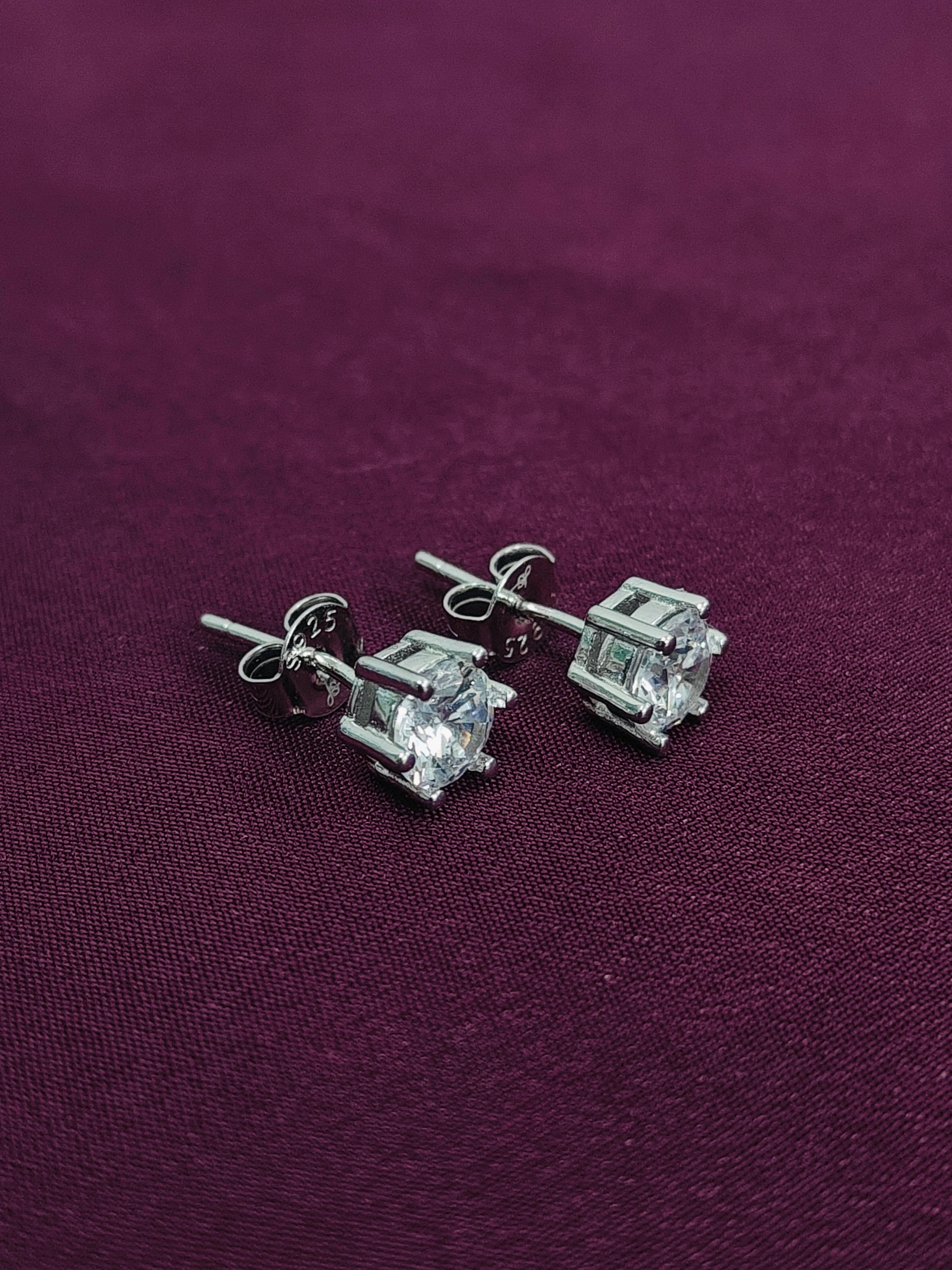 Silver square-cut stud earrings on a purple fabric background