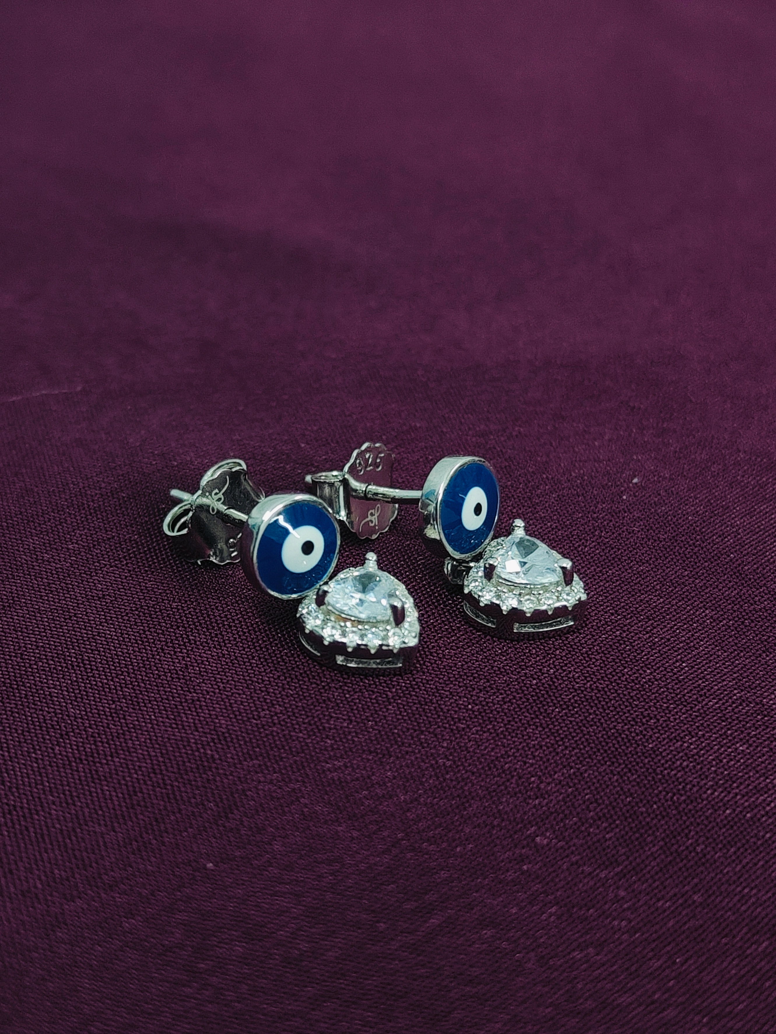 Pair of silver earrings with blue and white designs on a purple fabric background