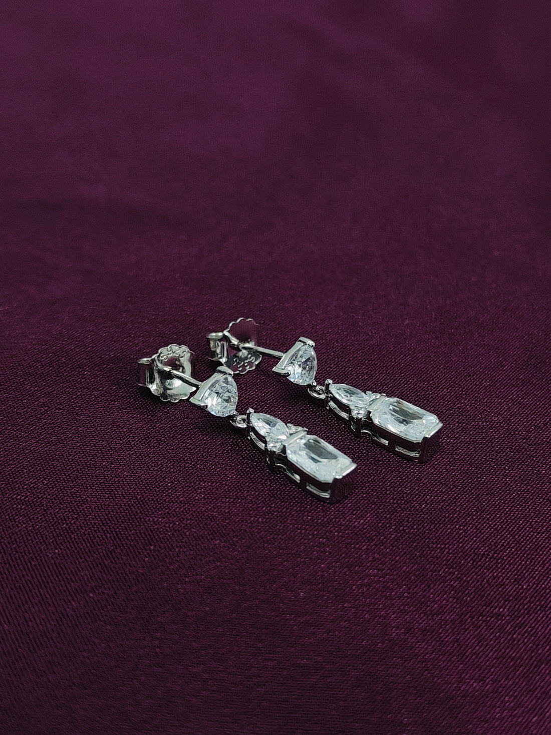 Silver earrings with clear stones on a purple fabric background