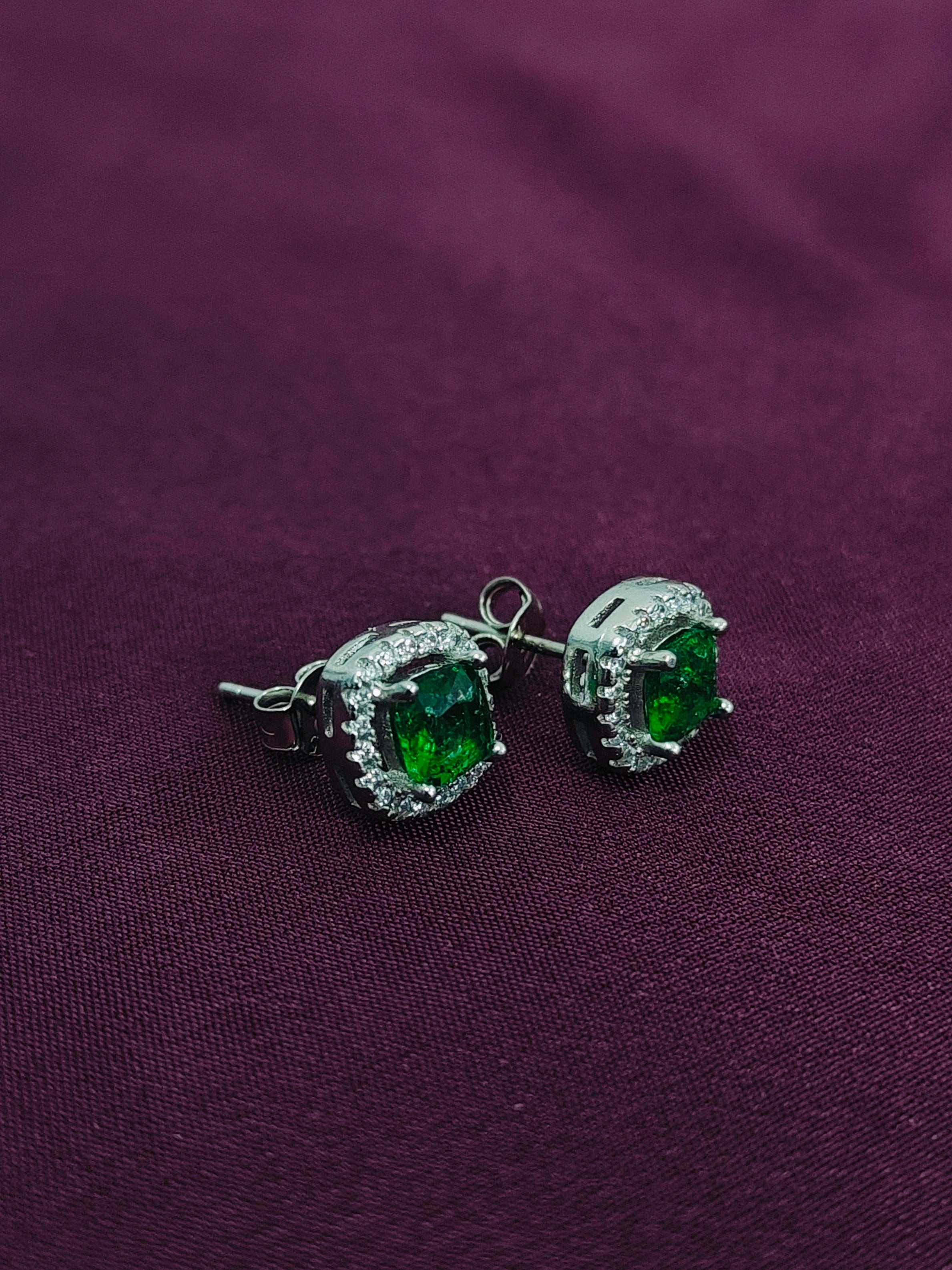 Pair of green gemstone earrings on a purple fabric background
