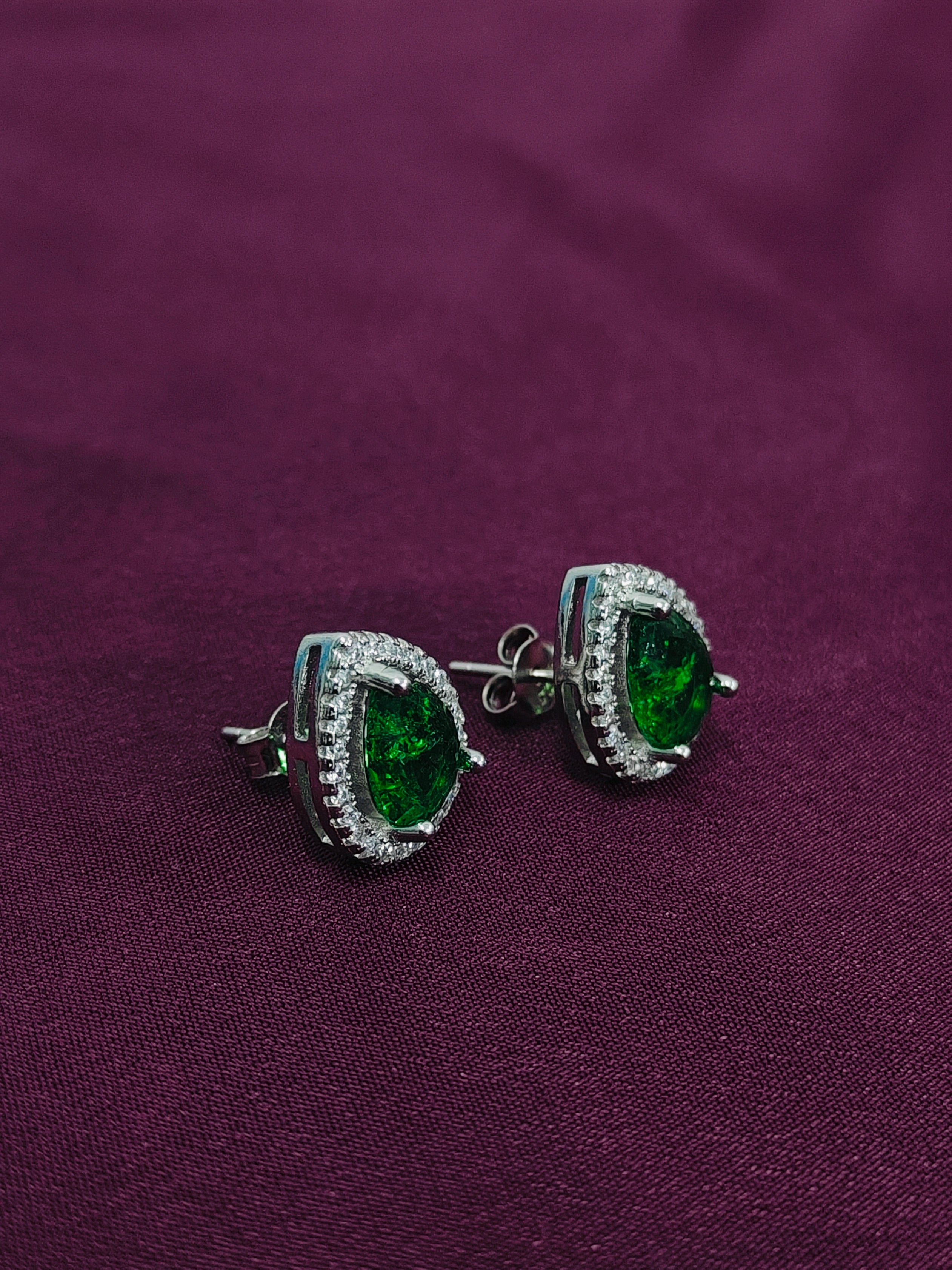 Green gemstone earrings with silver setting on a purple fabric background