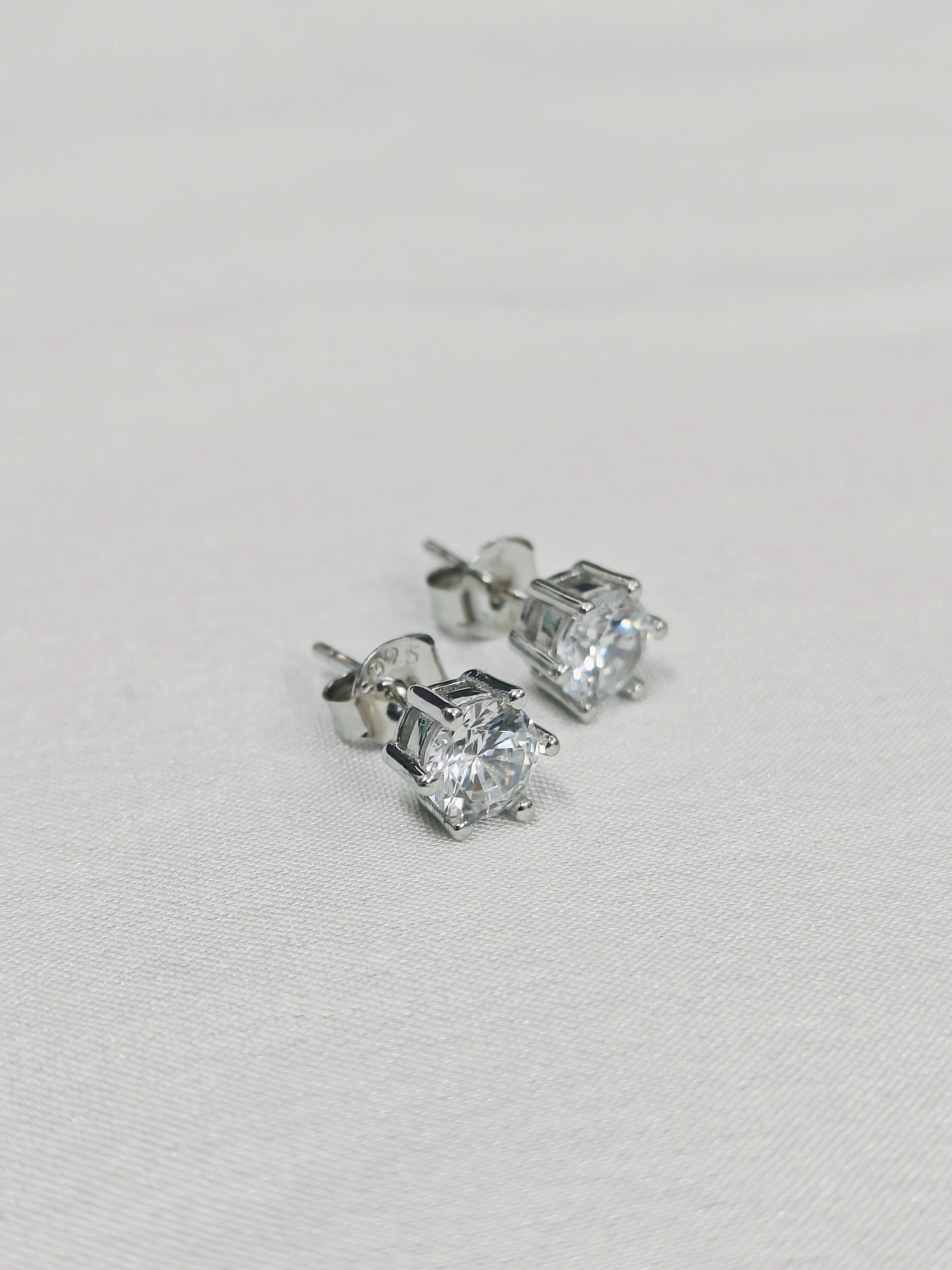 Pair of silver stud earrings with clear gemstones on a light gray background