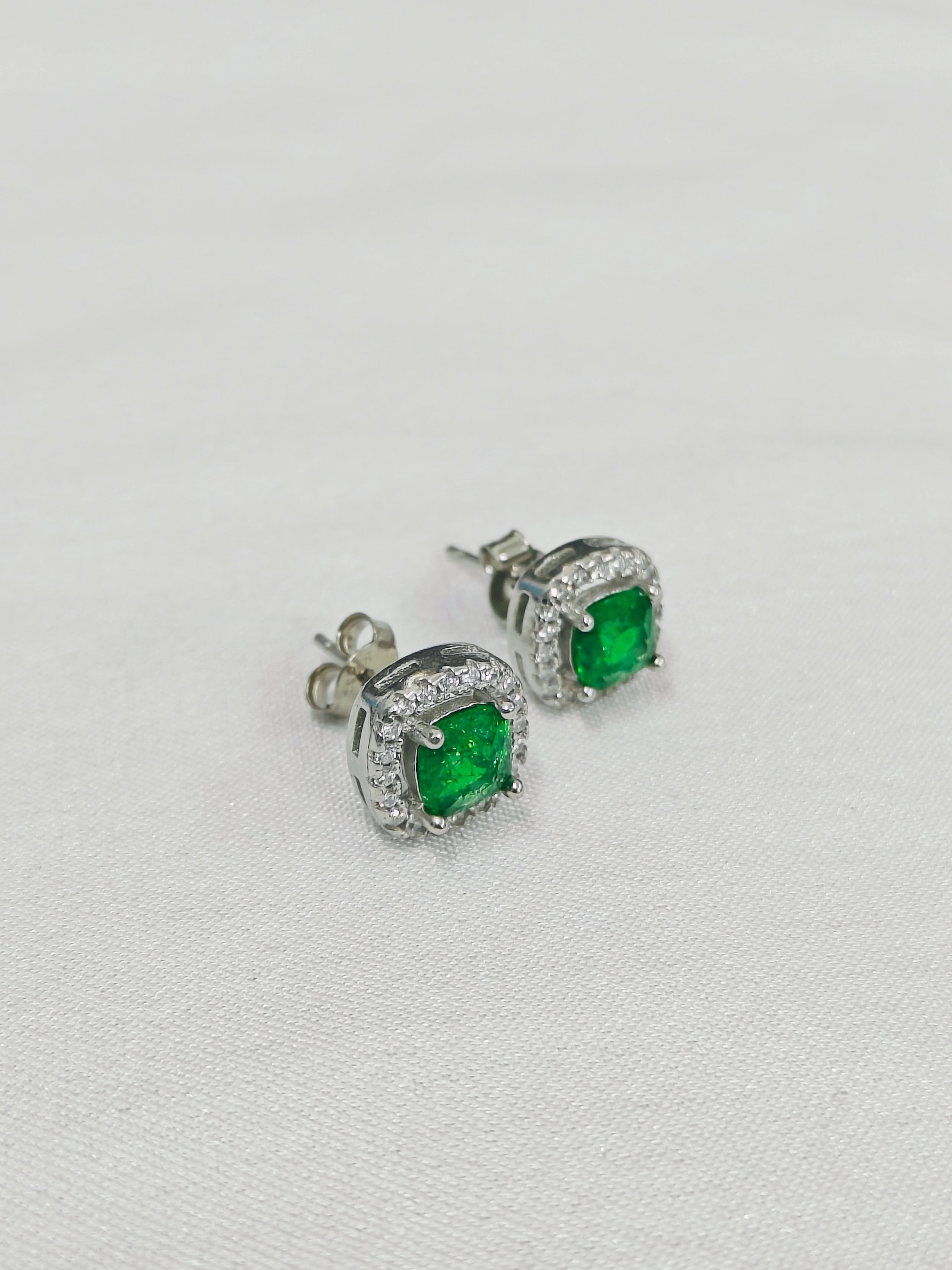 Pair of emerald green stud earrings on a light gray background