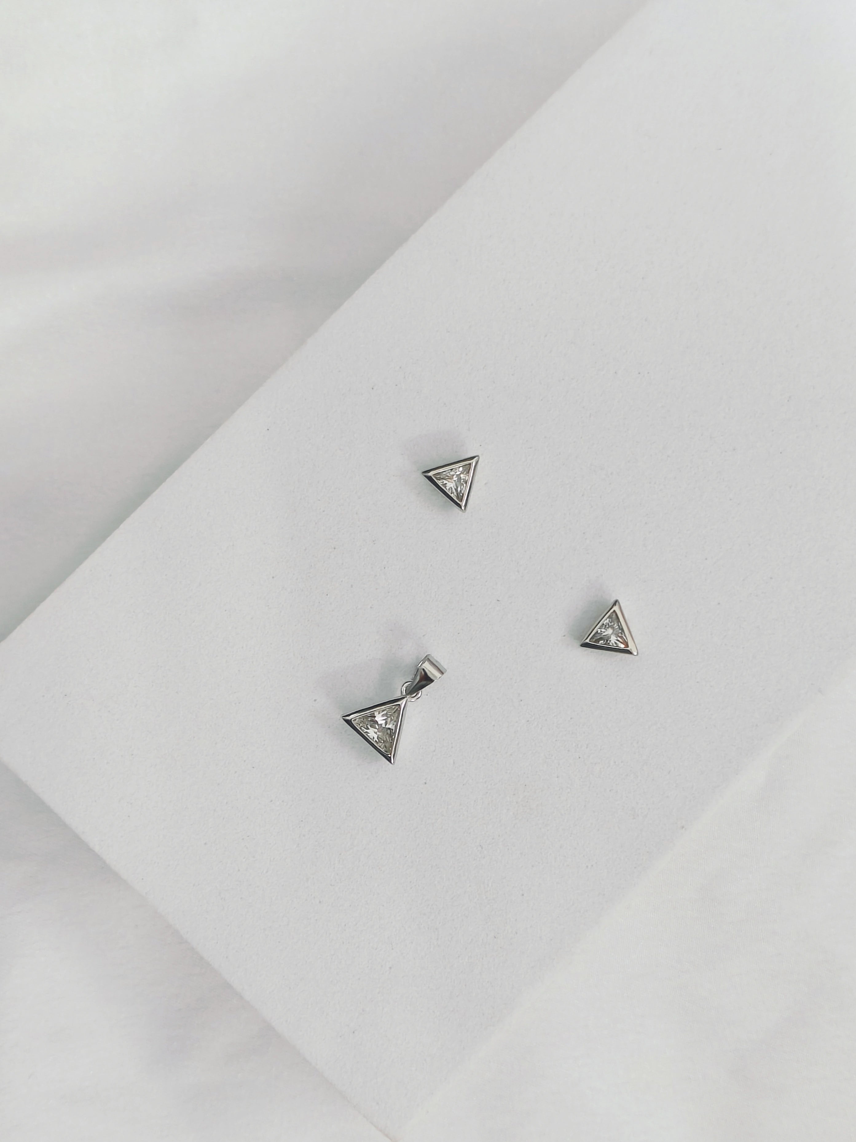 Three silver triangle-shaped earrings on a light gray surface