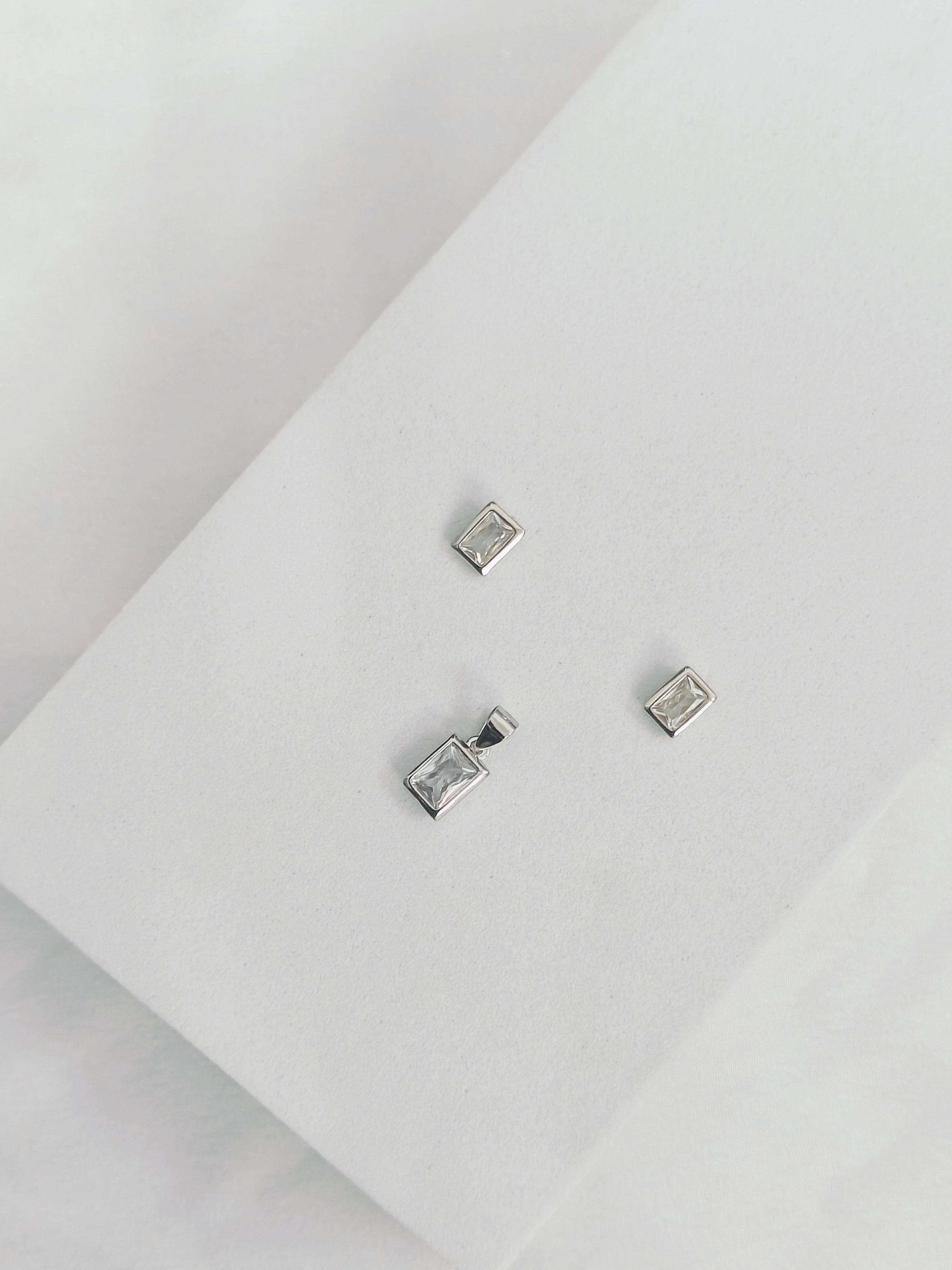 Silver rectangular stud earrings on a light gray surface