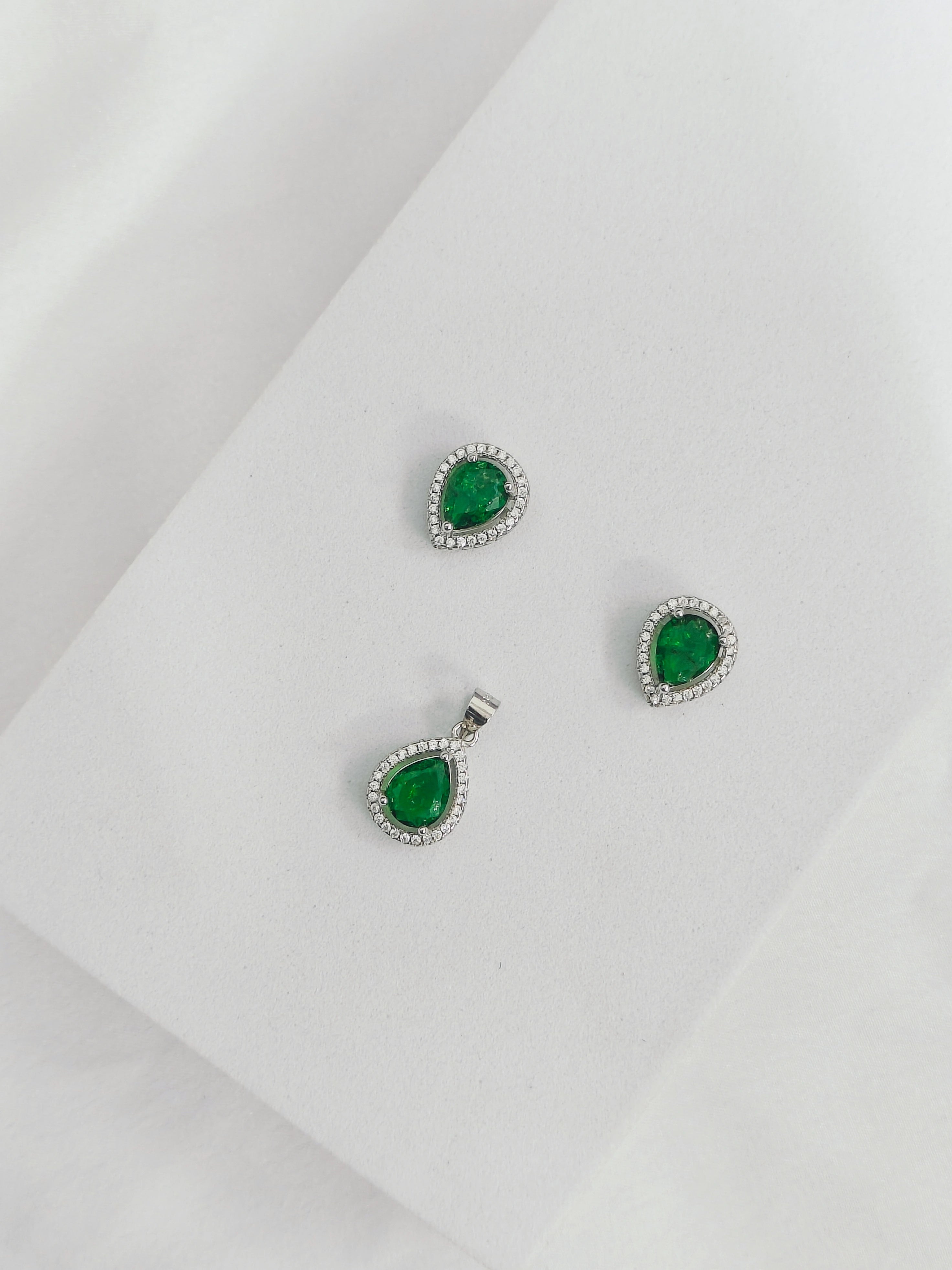 Jewelry set with emerald green gemstones and silver settings on a light gray background