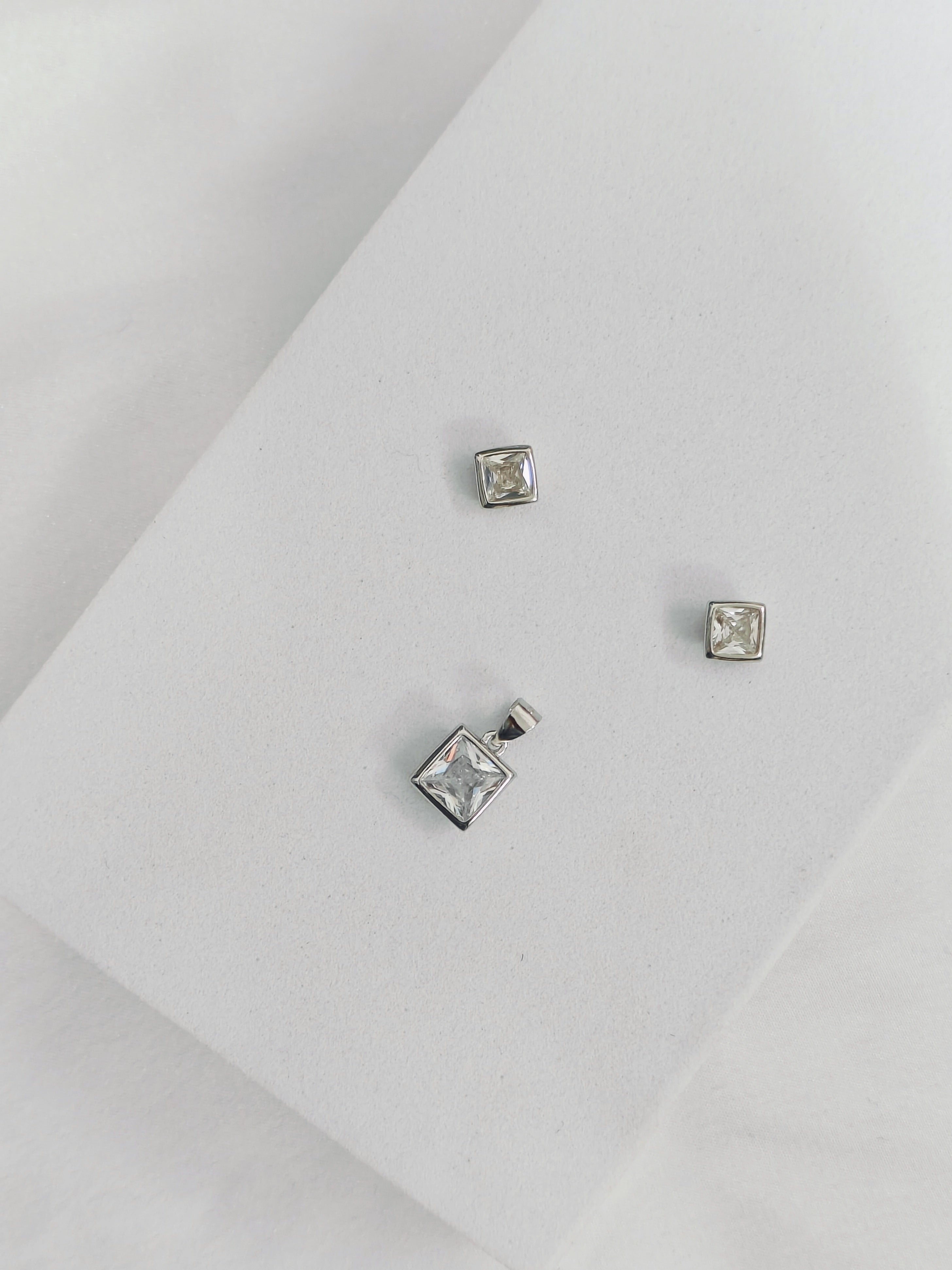 Set of silver square-shaped earrings on a light gray background