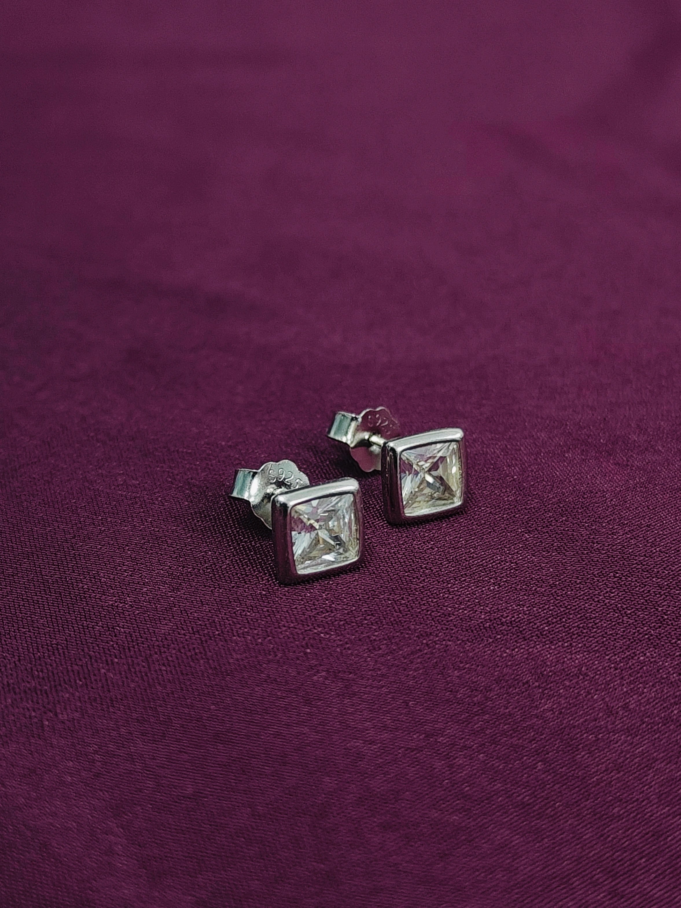 Silver square stud earrings on a purple fabric background