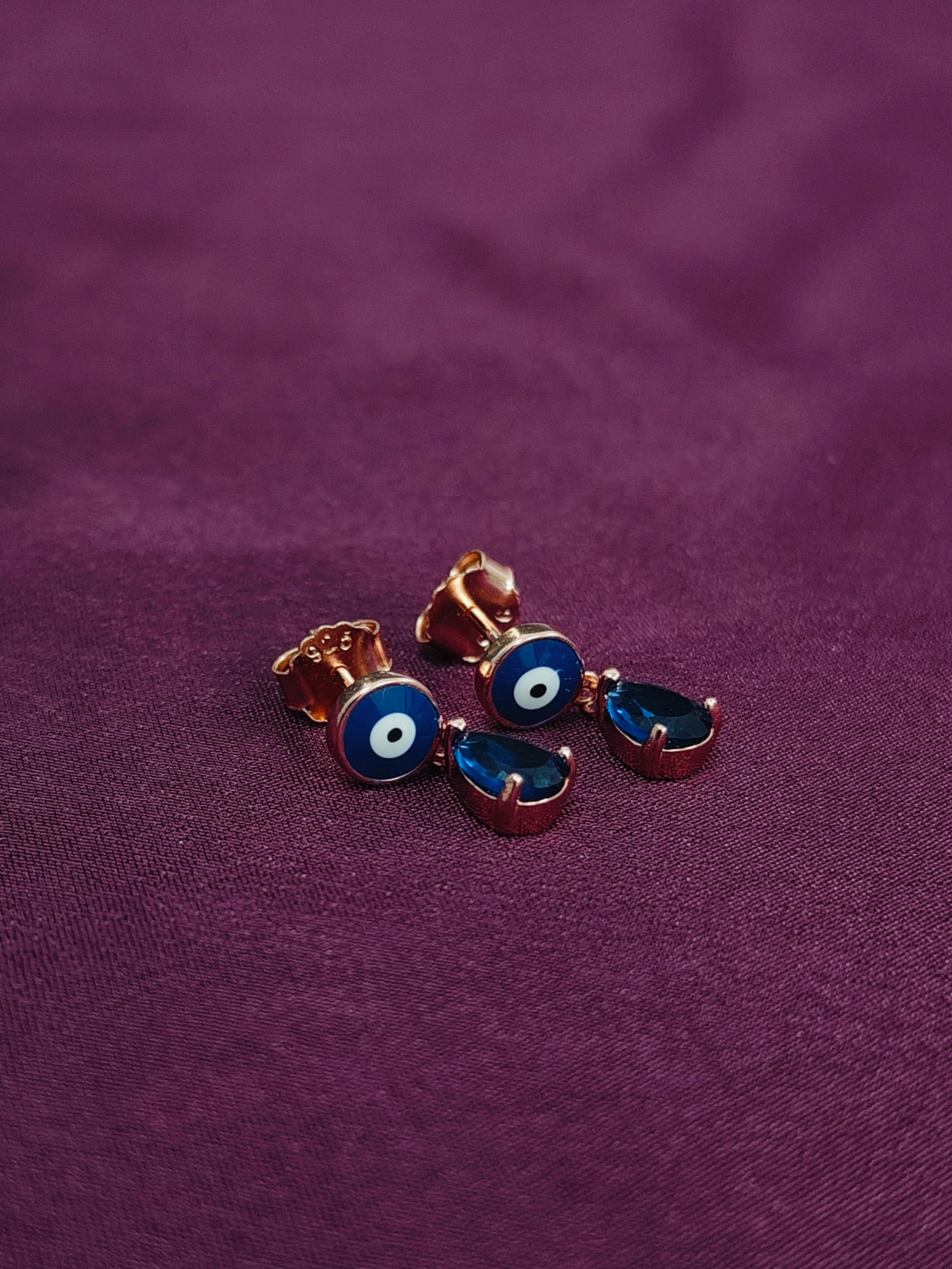 Pair of blue evil eye earrings on a purple fabric background