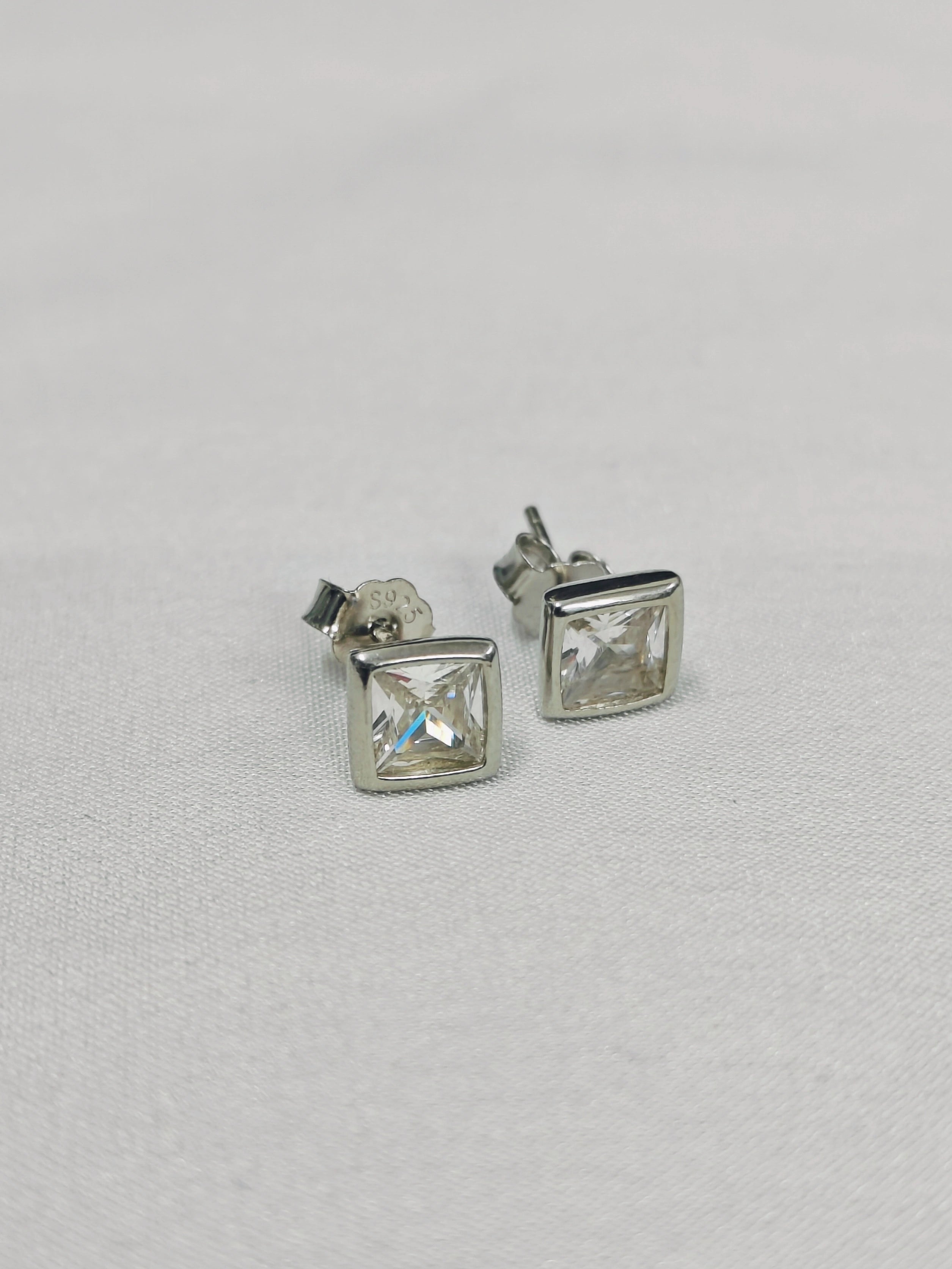 Pair of silver square stud earrings on a light gray background