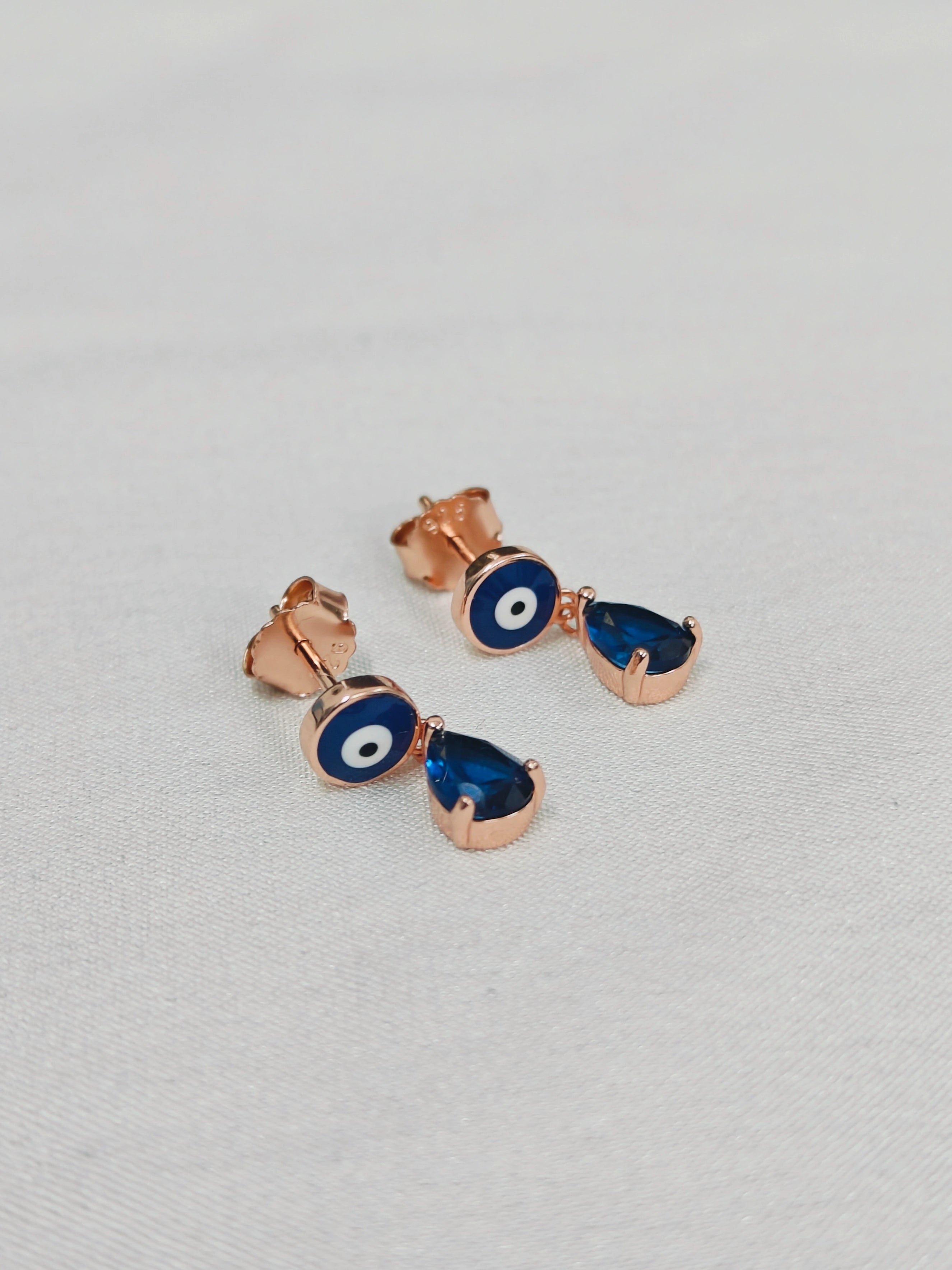 Pair of rose gold earrings with blue gemstones on a light gray background