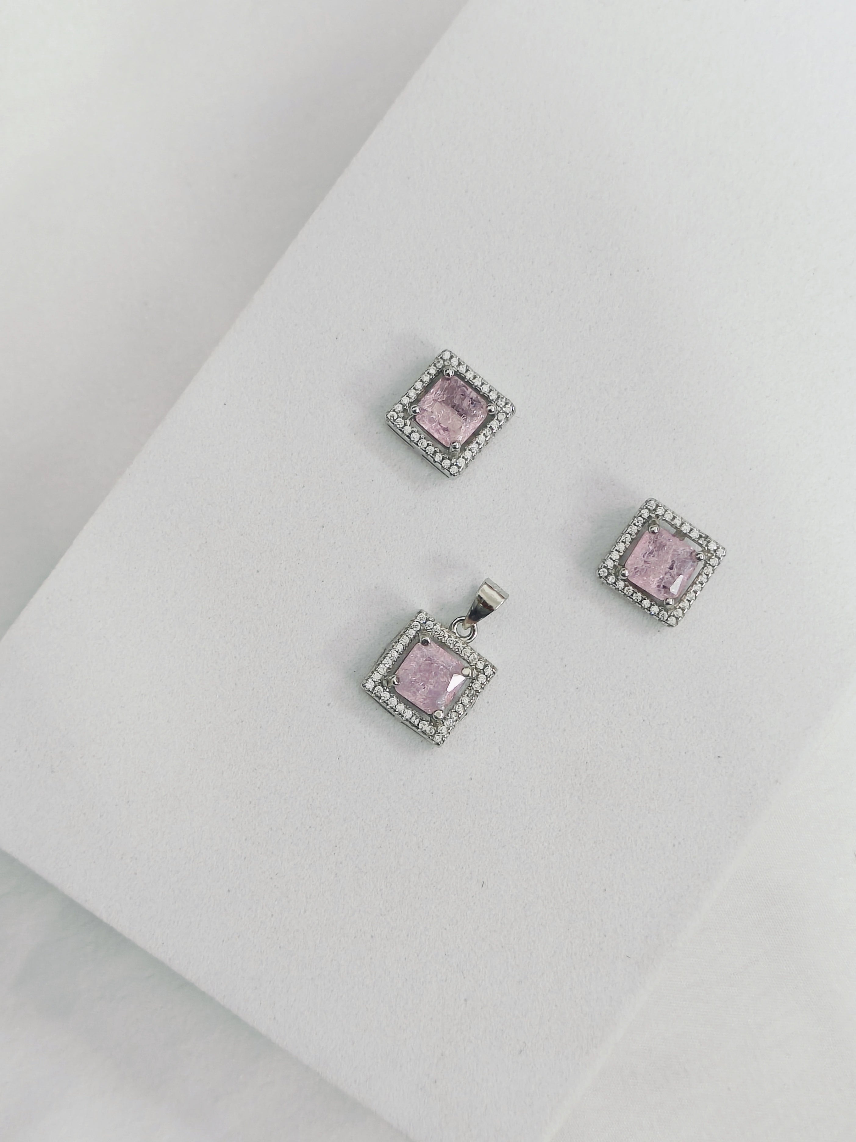 Jewelry set with pink square stones and silver frames on a white surface