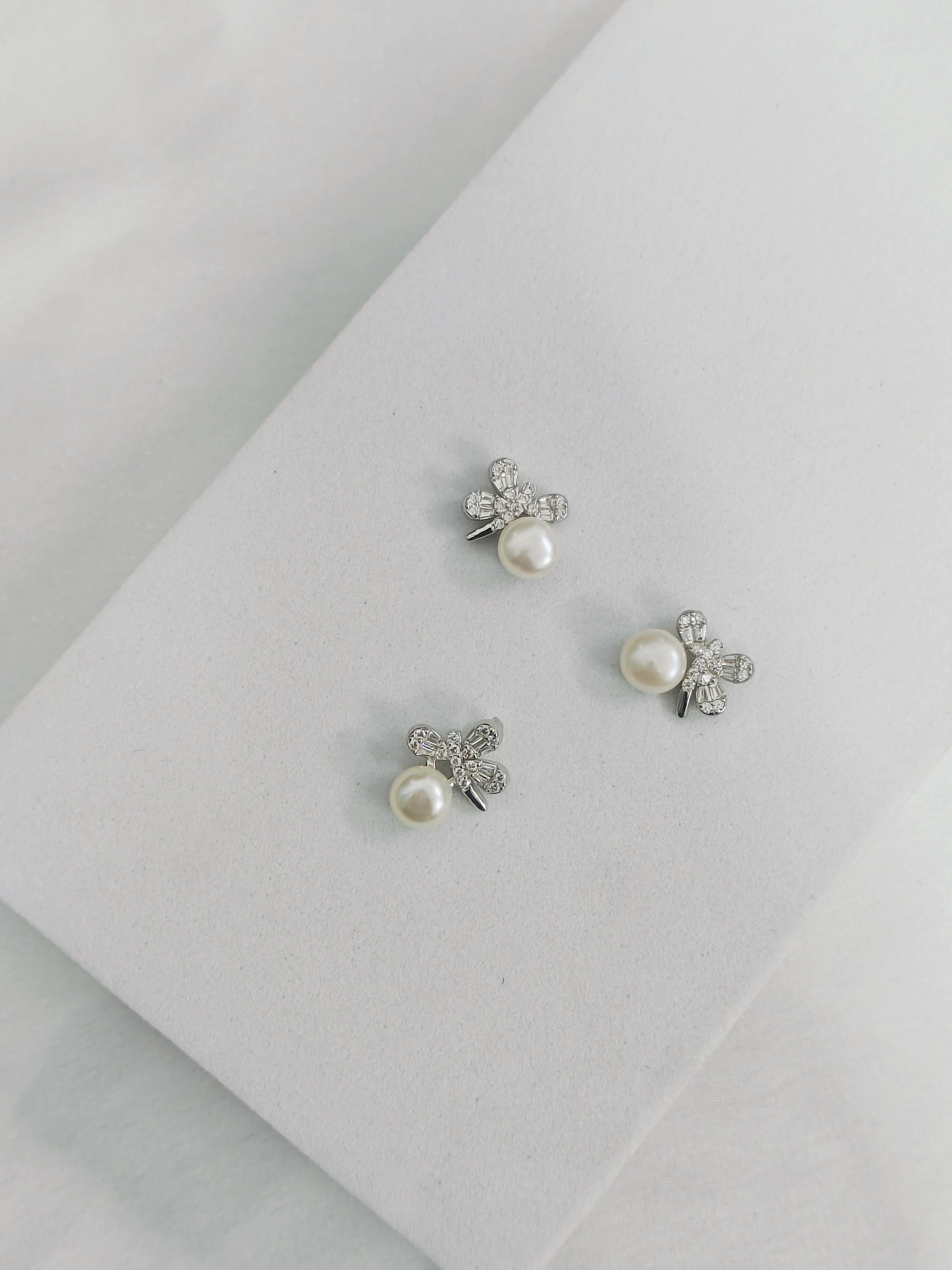 Pair of pearl earrings with silver butterfly designs on a light gray background