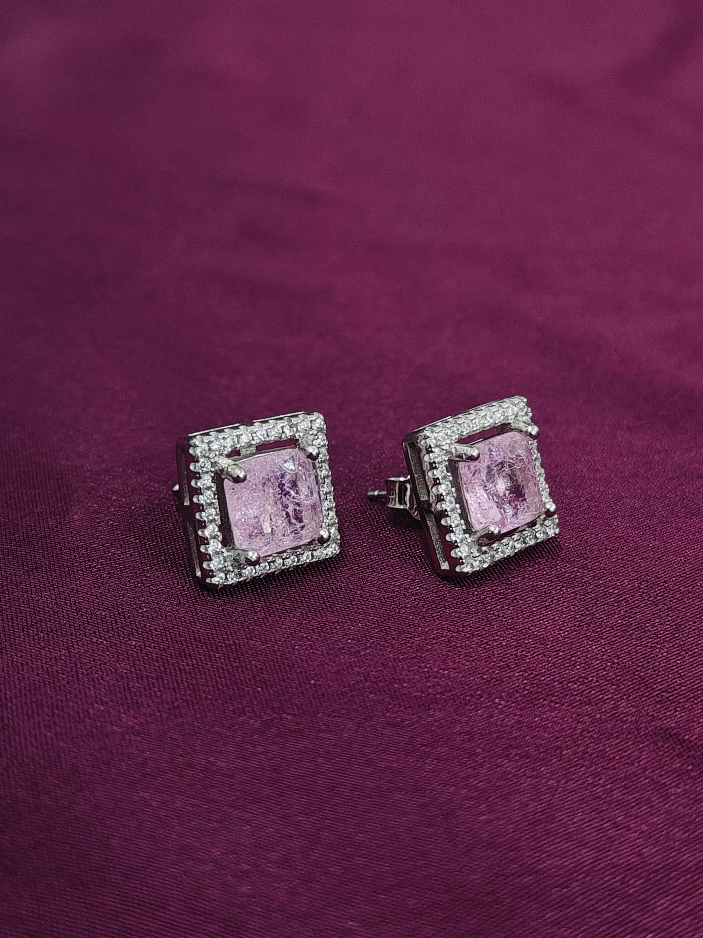 Pair of pink square gemstone earrings with silver accents on a purple fabric background