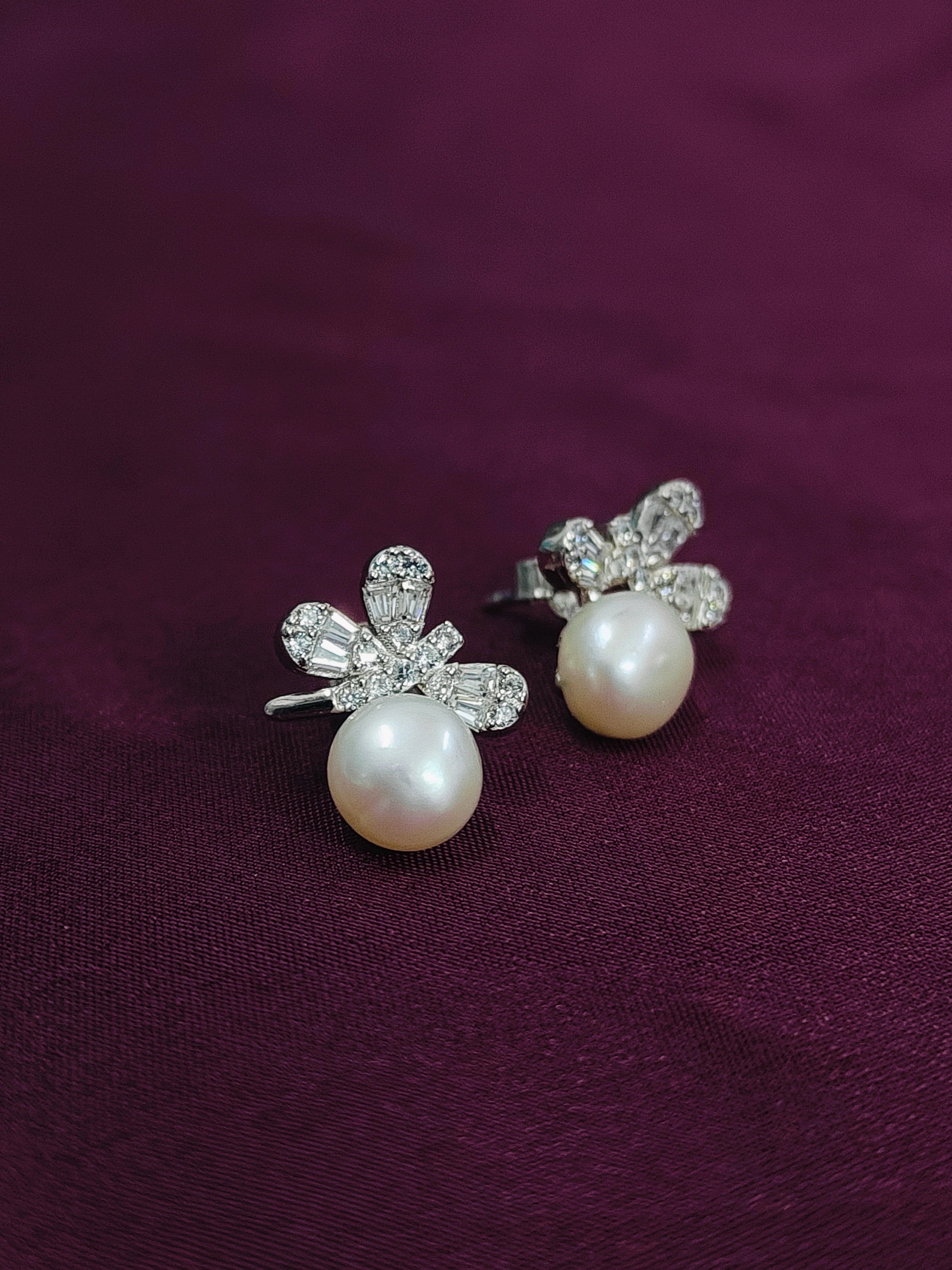 Pearl earrings with floral designs on a purple fabric background