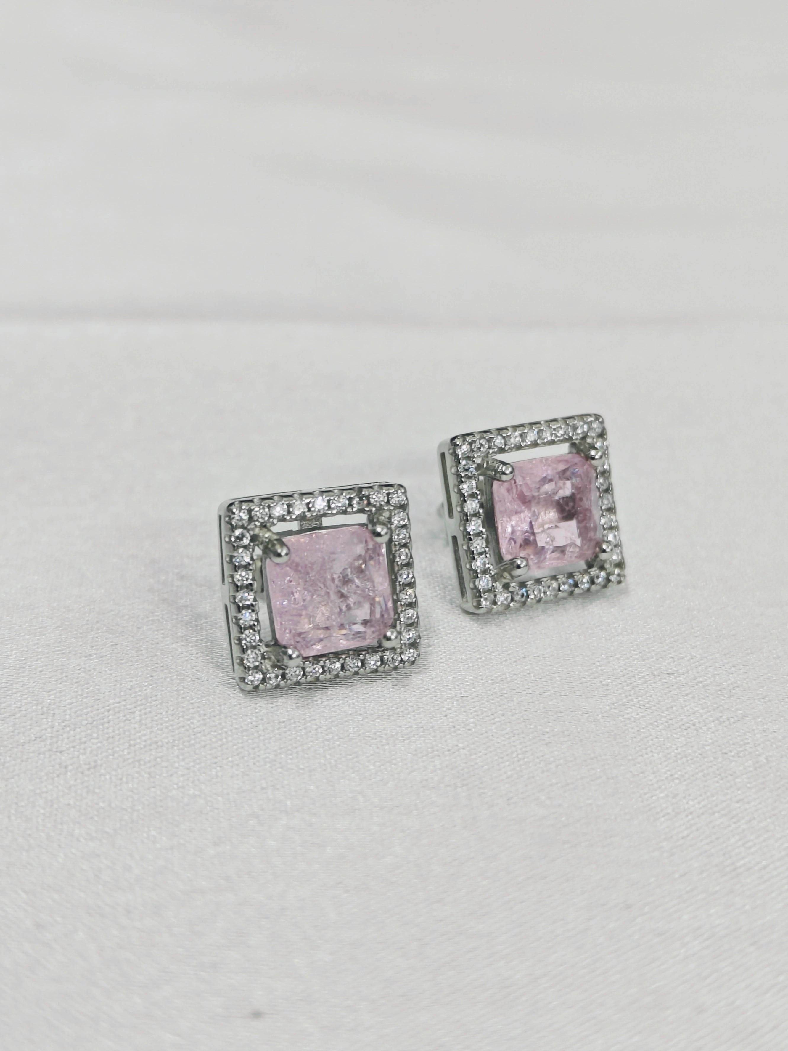 Pair of square-shaped earrings with pink gemstones on a light gray background