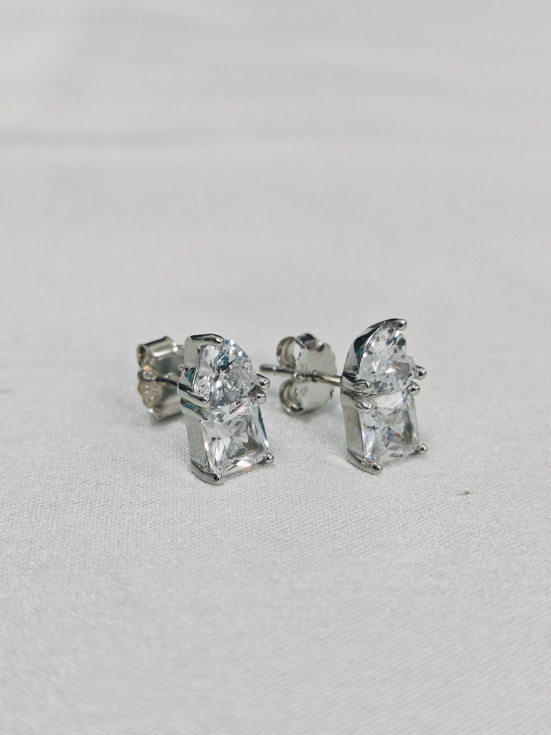 Pair of silver stud earrings with clear gemstones on a light gray background