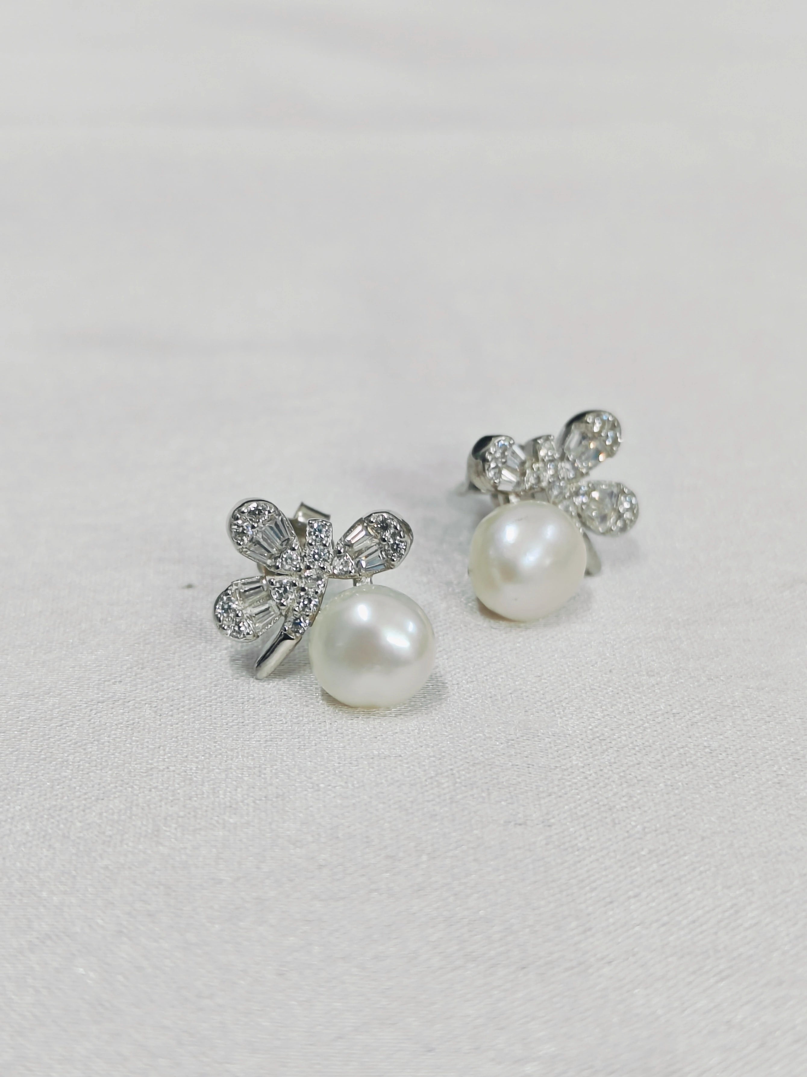 Pair of pearl earrings with silver butterfly designs on a light gray background
