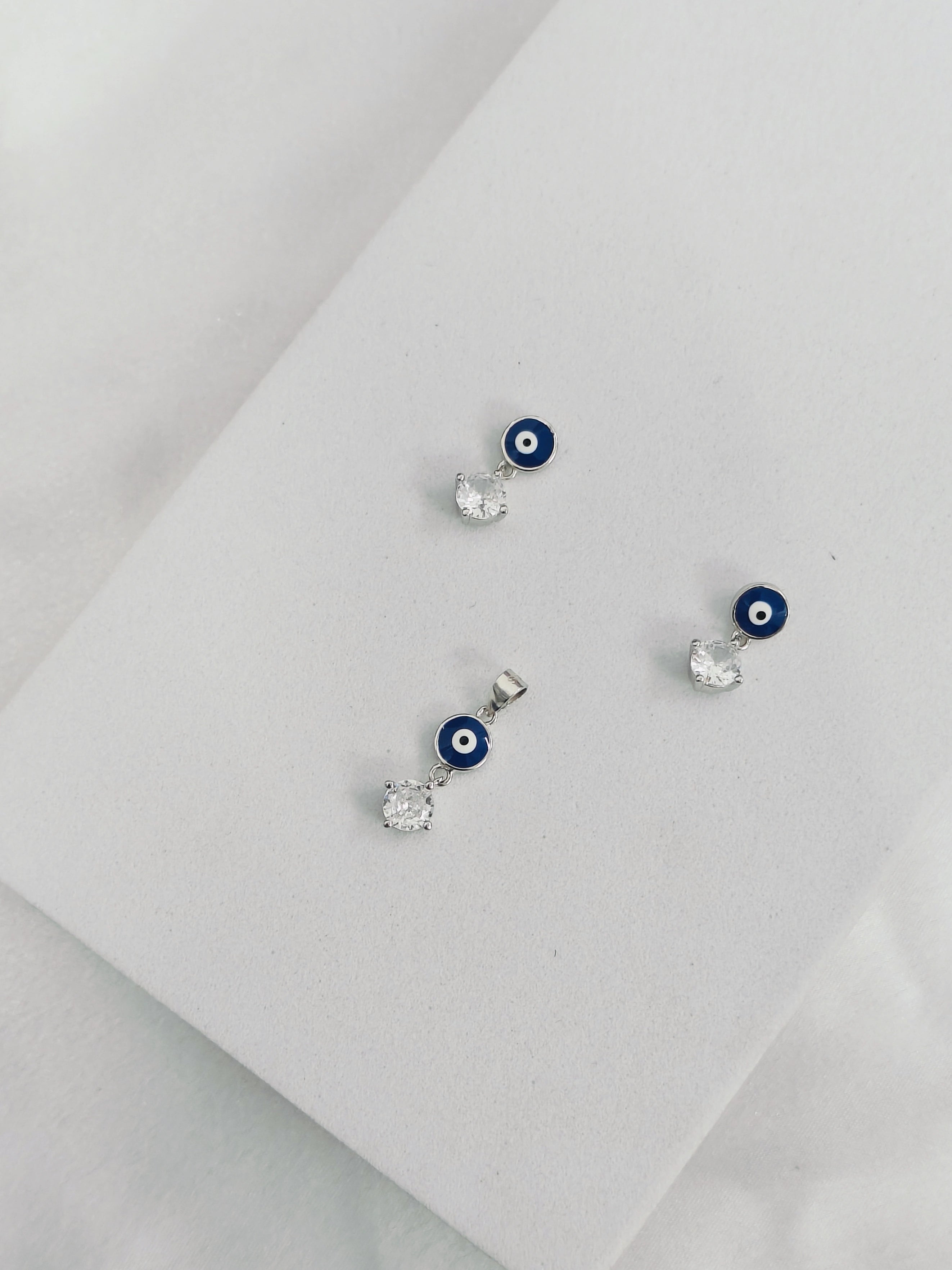 Pair of earrings with blue evil eye design on a light gray background