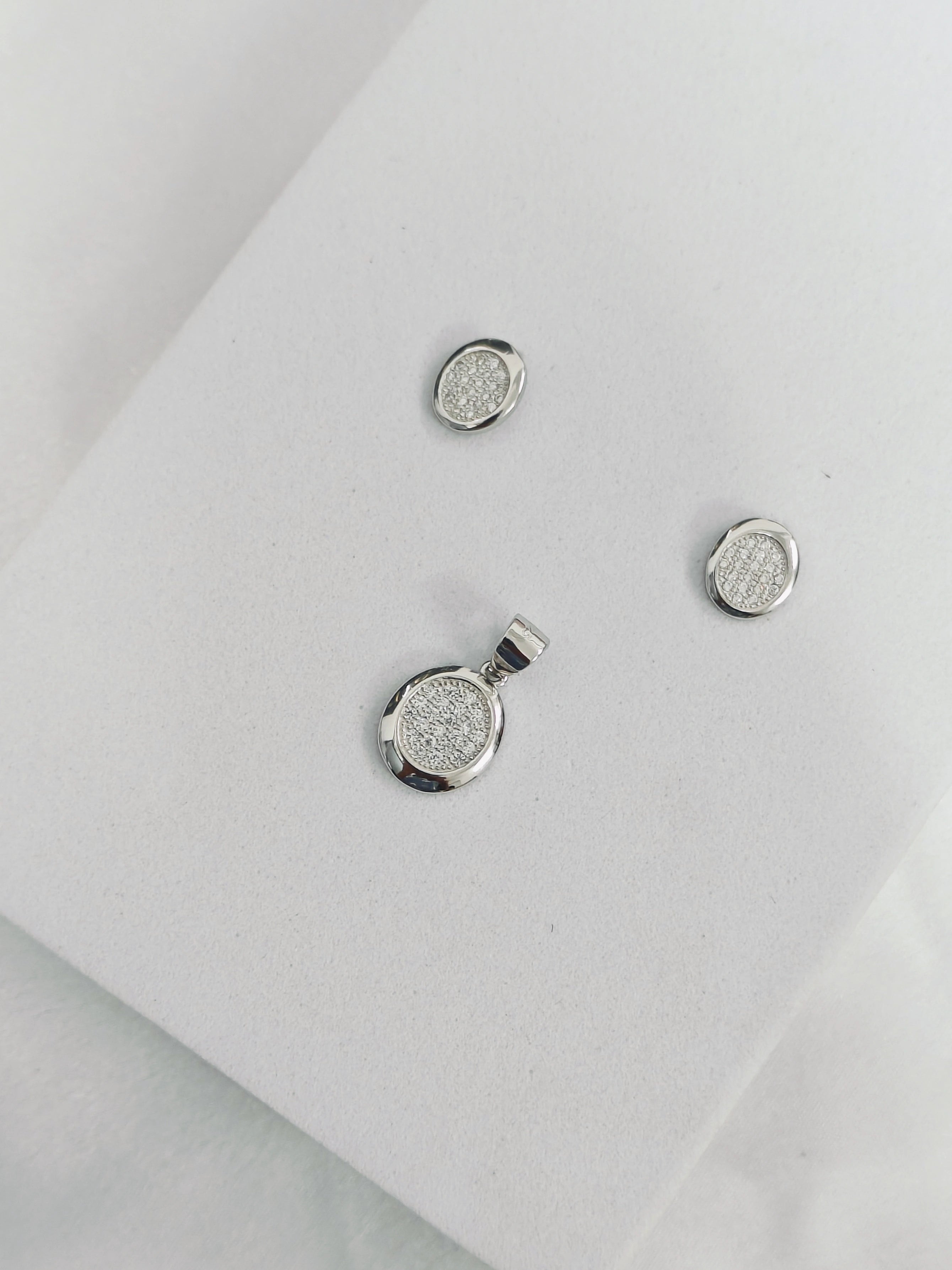 Silver jewelry set with pendant and earrings on a light gray background