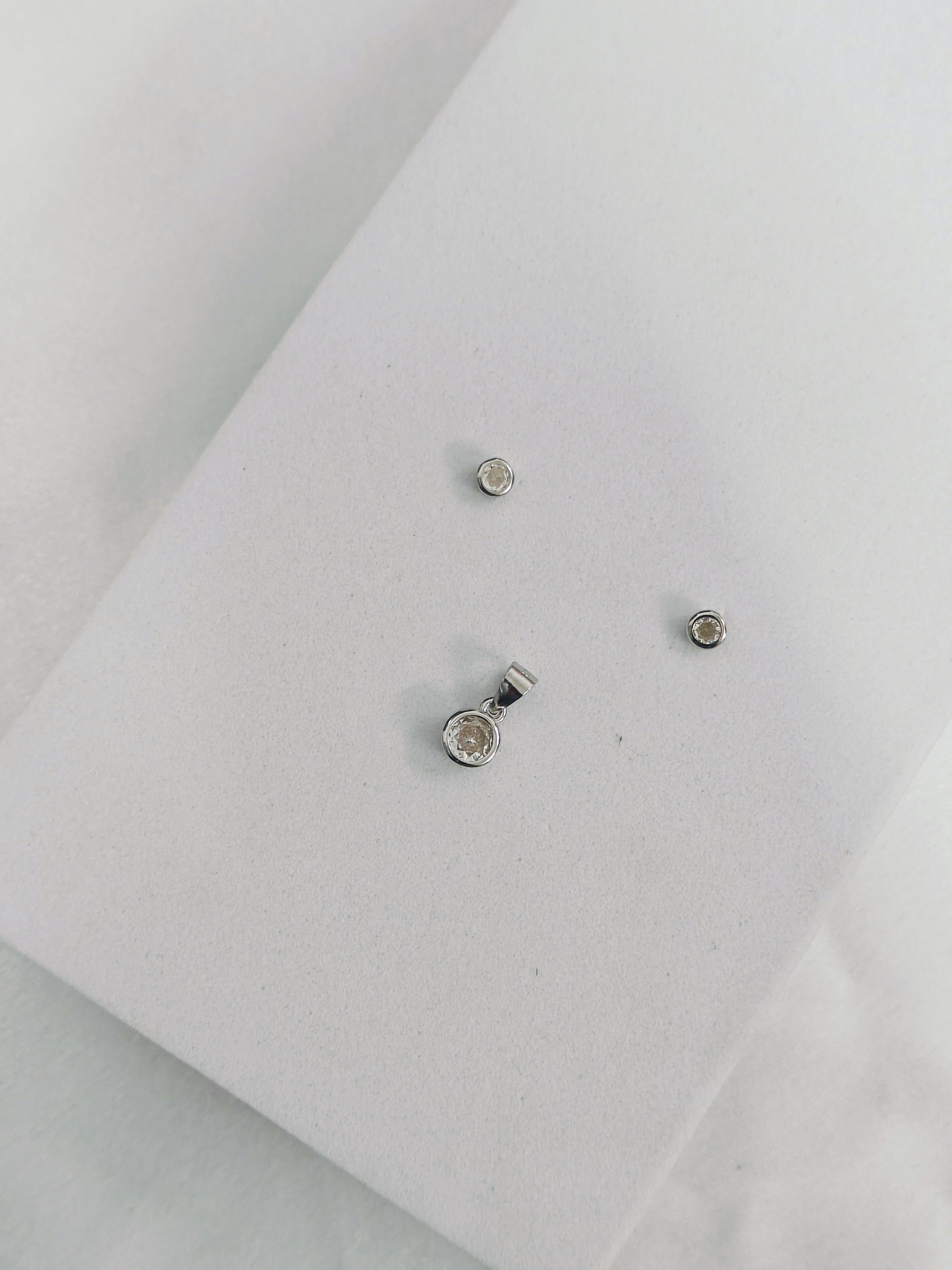 Two small silver earrings on a light gray background