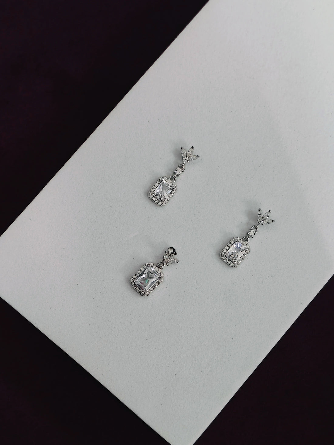 Pair of silver earrings on a white card with a black background