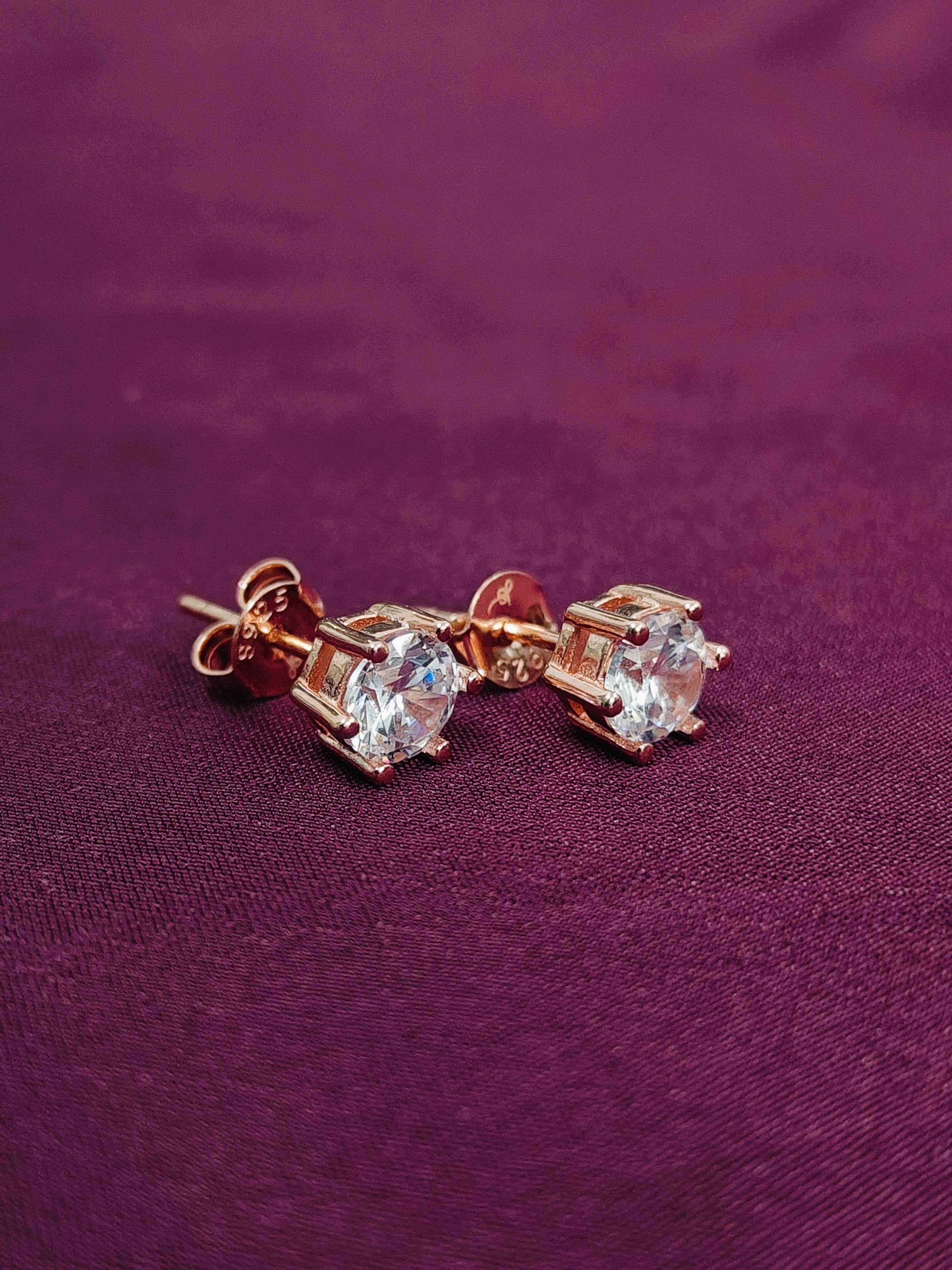 Pair of rose gold earrings with clear gemstones on a purple fabric background