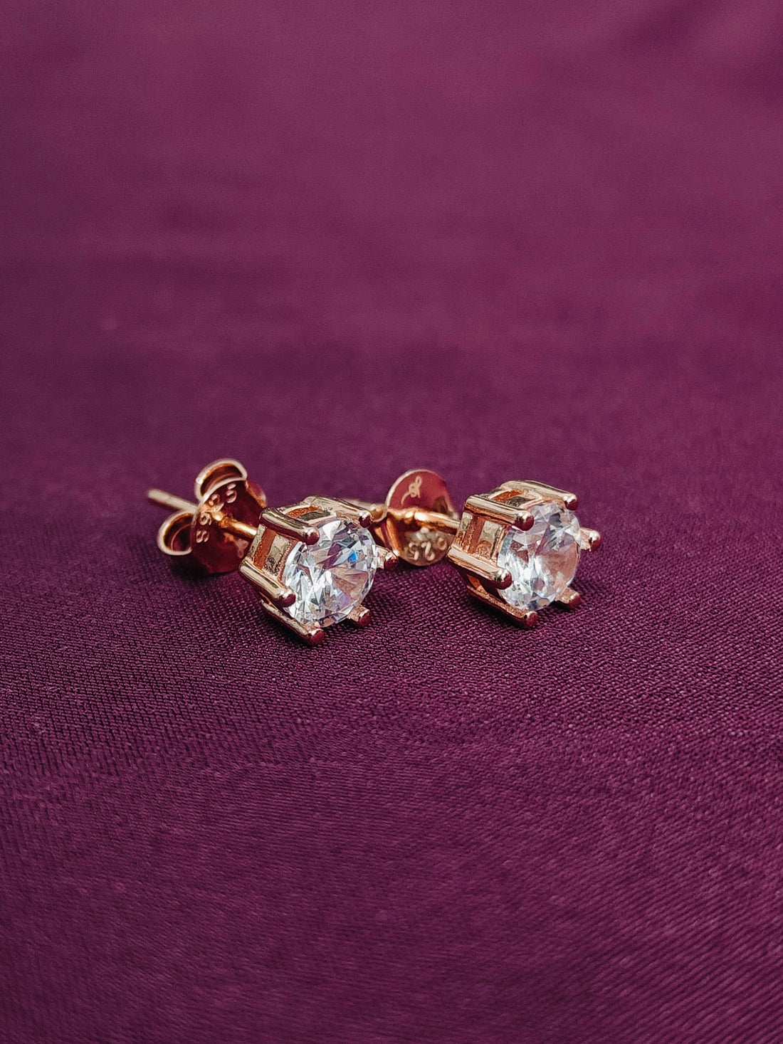 Pair of rose gold earrings with clear gemstones on a purple fabric background