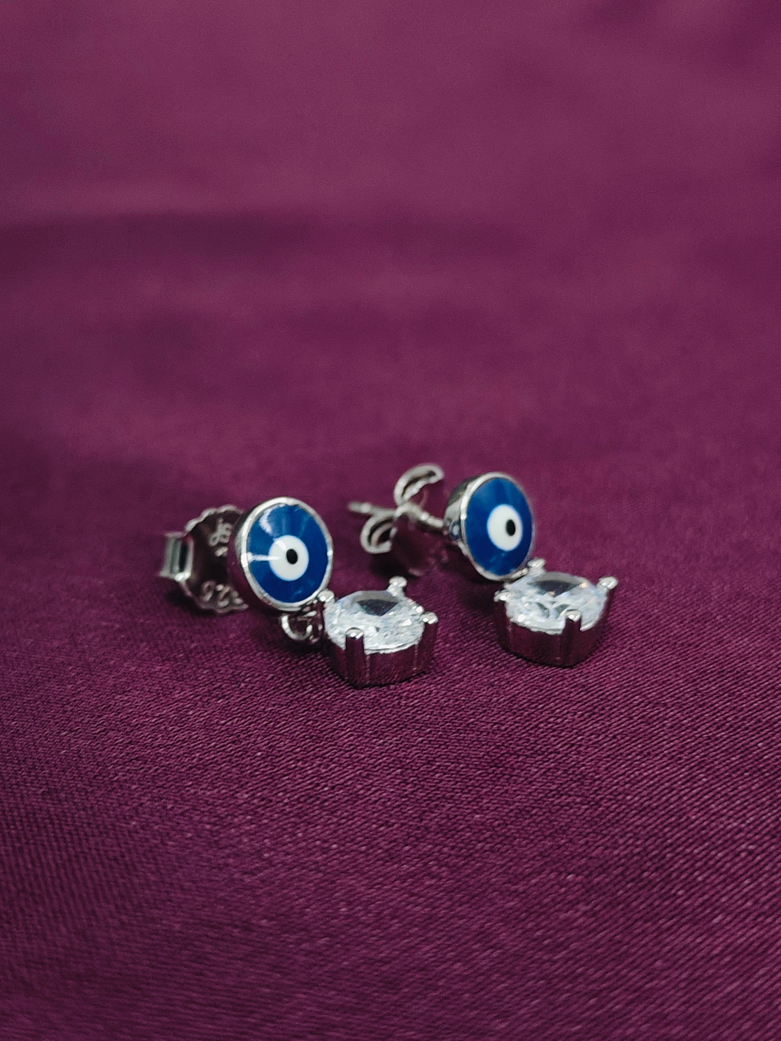 Silver earrings with blue and white eye design on a purple fabric background