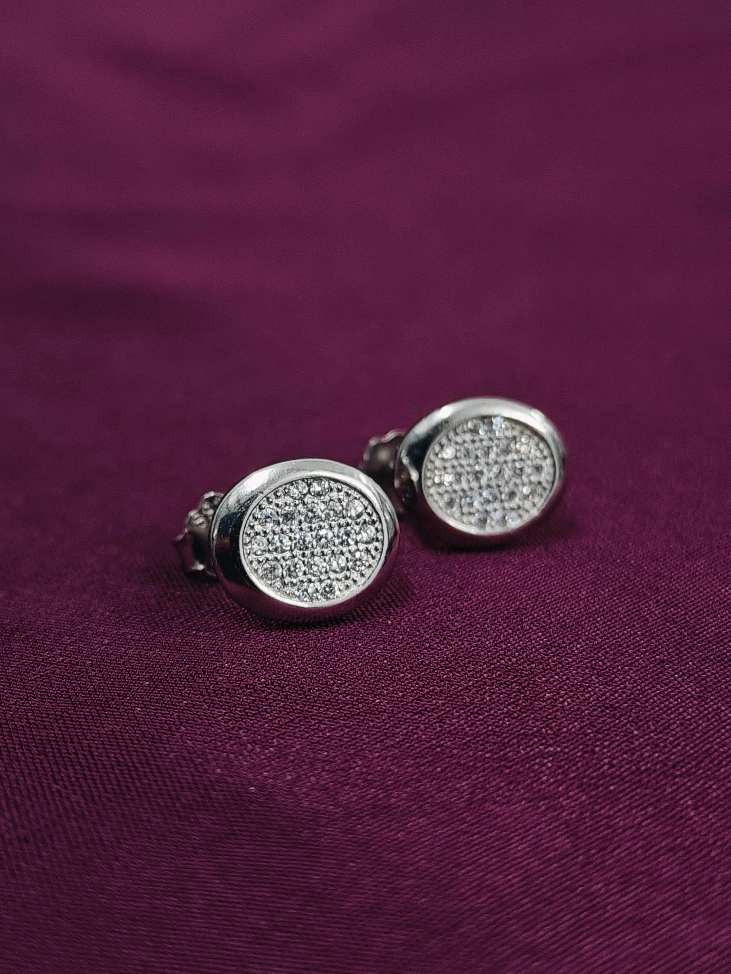 Silver stud earrings with a sparkling design on a purple fabric background