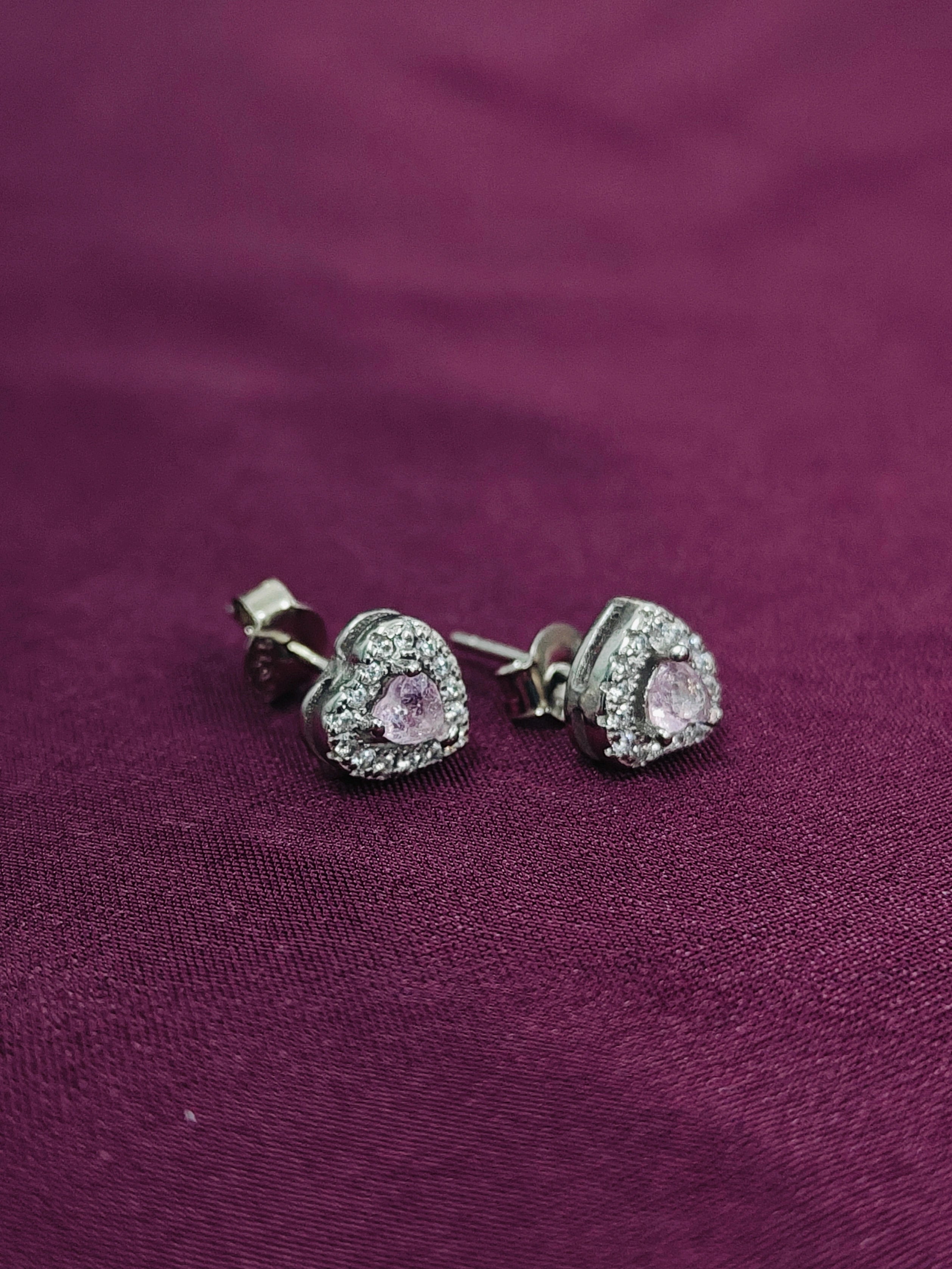 Heart-shaped earrings with pink gemstones on a purple fabric background