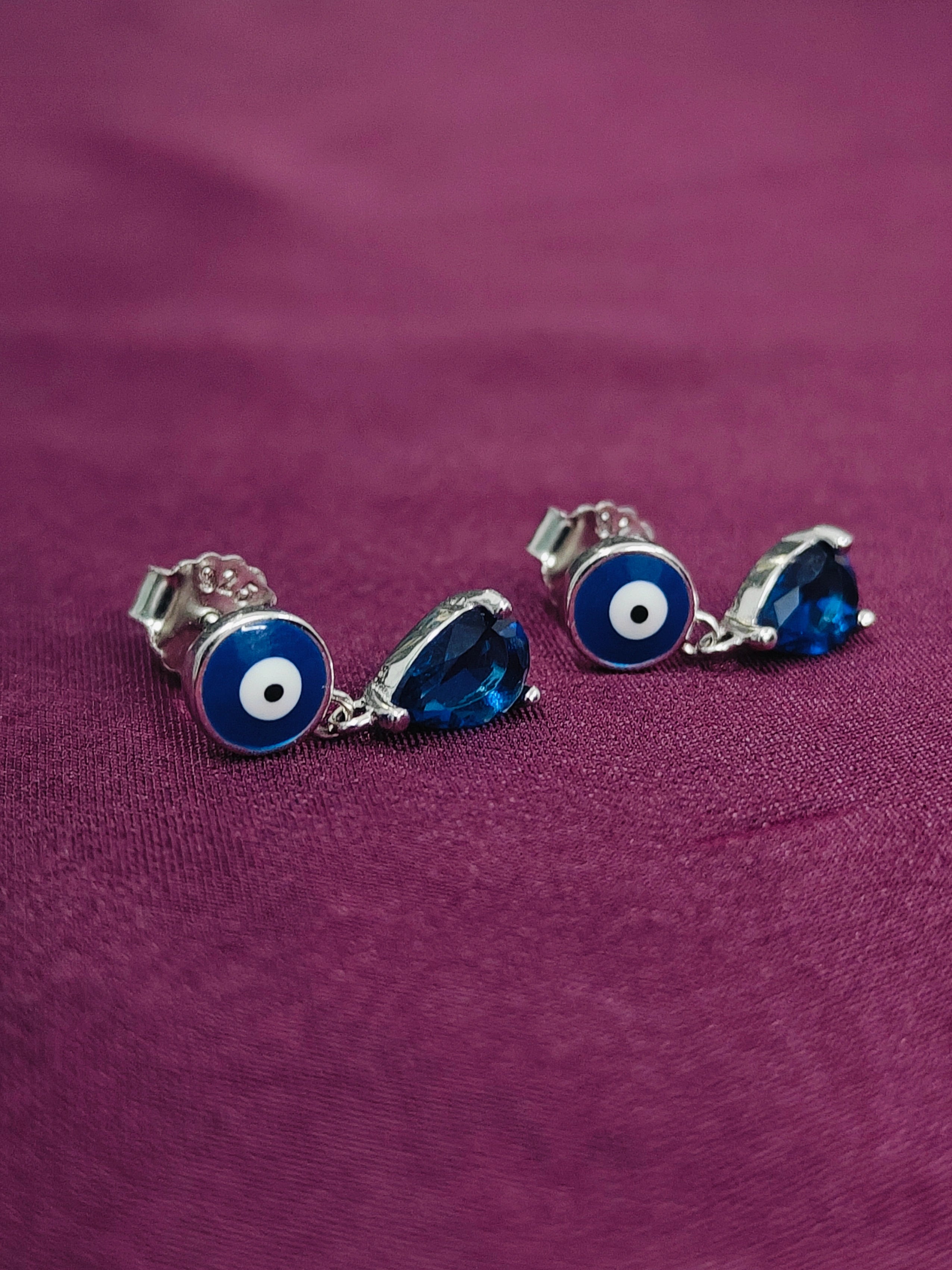 Pair of blue evil eye earrings on a purple fabric background