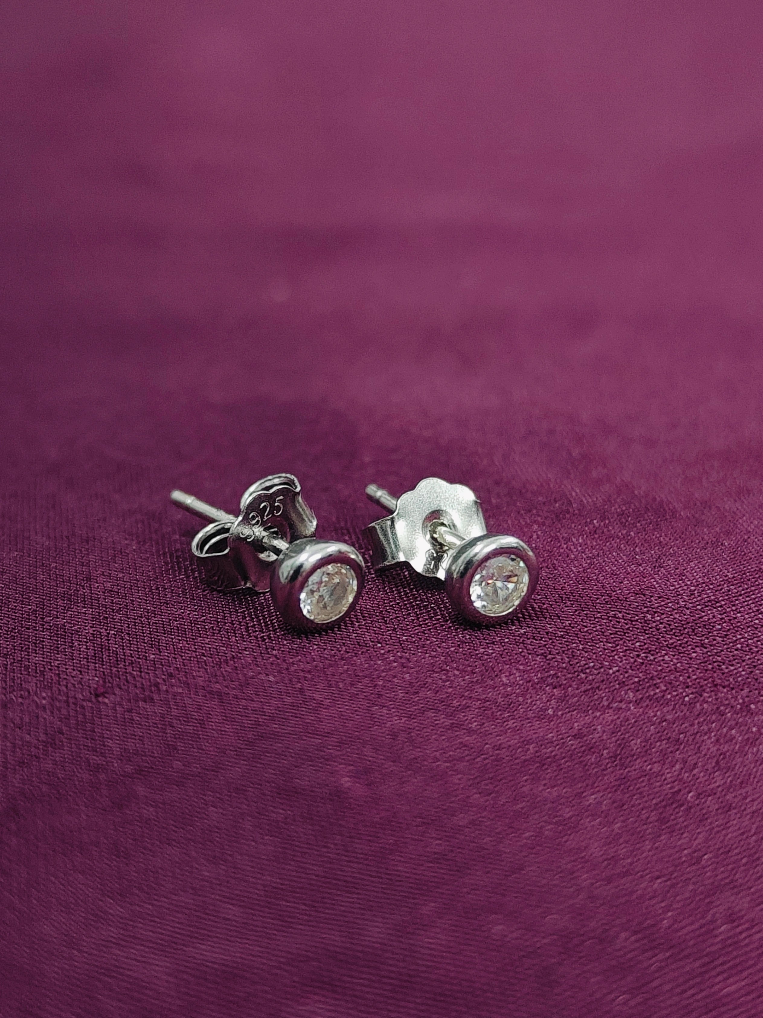 Silver stud earrings with clear gemstones on a purple fabric background