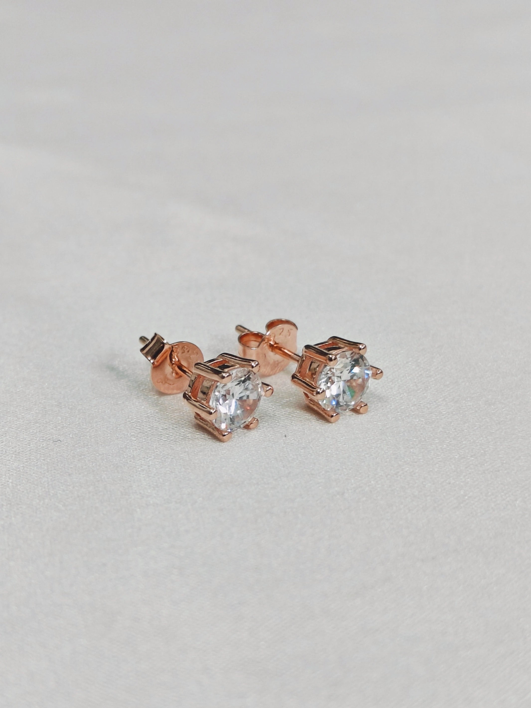 Rose gold stud earrings with clear gemstones on a light gray background