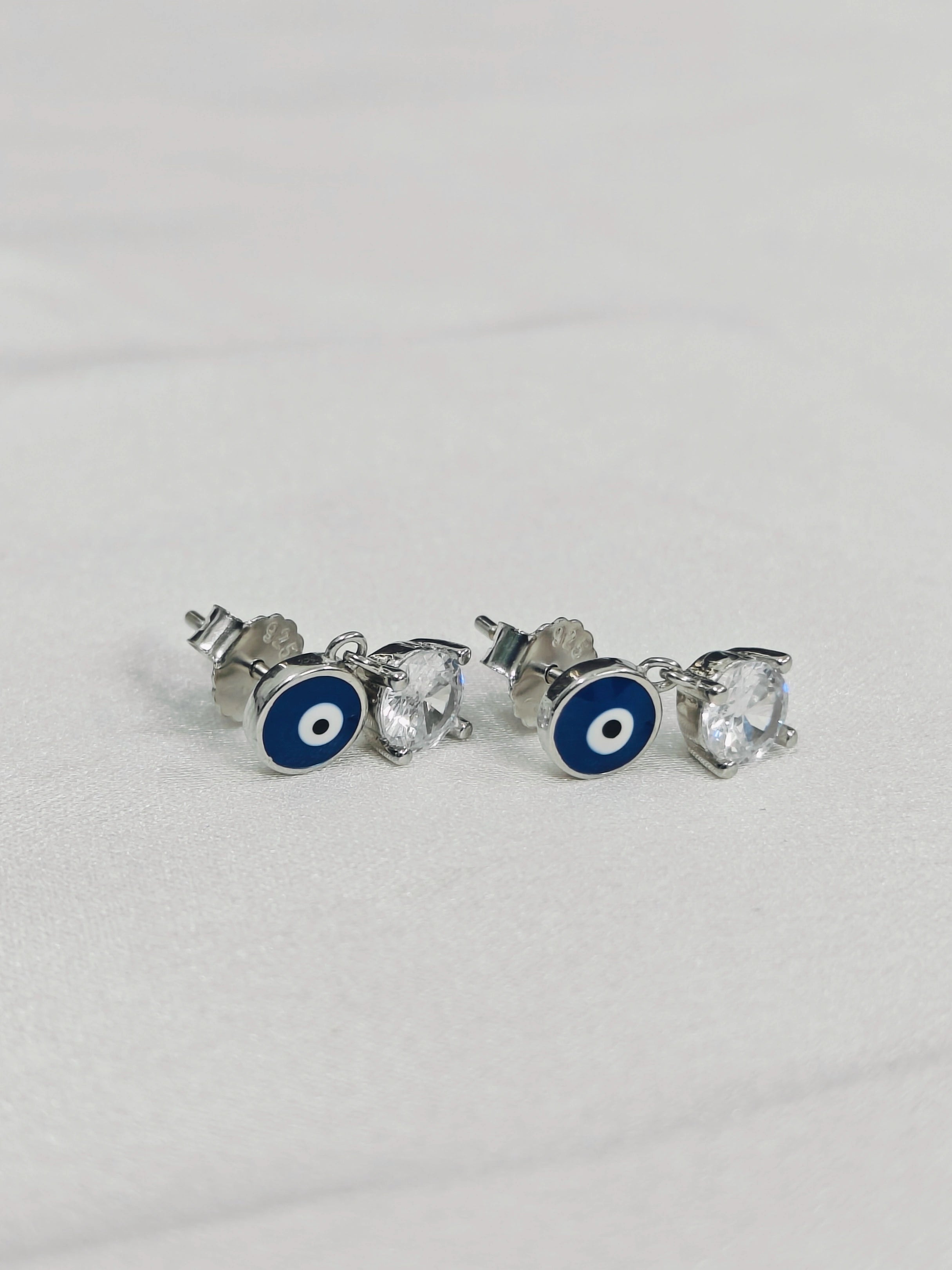 Pair of silver earrings with blue evil eye design on a light gray background