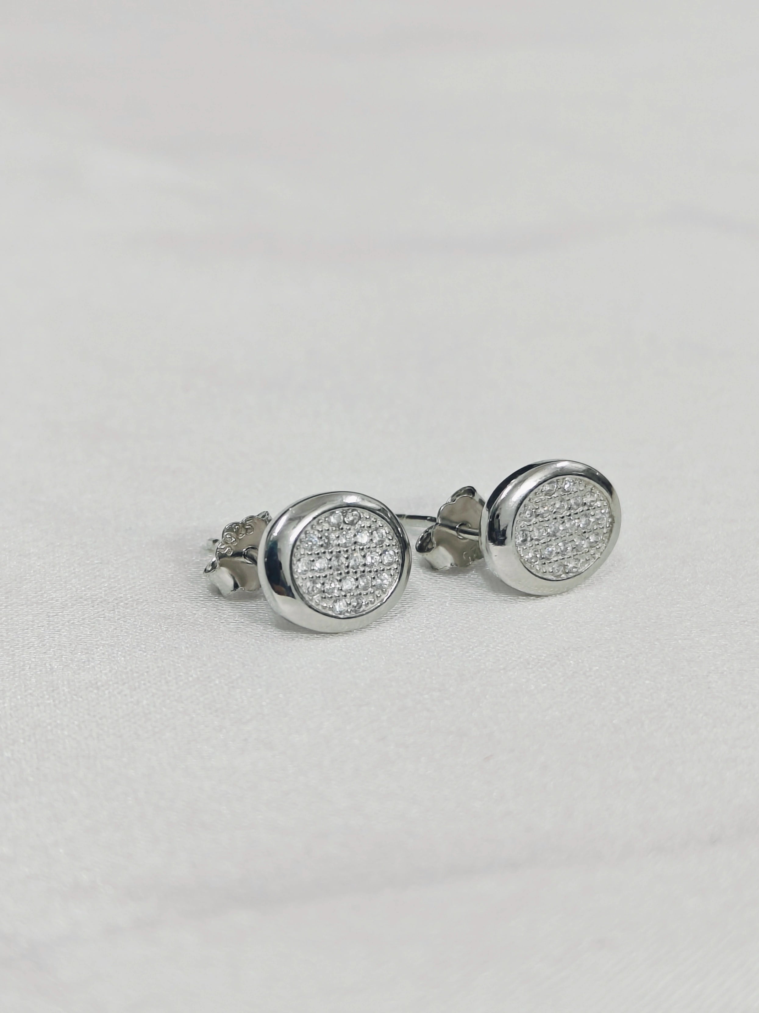 Silver round earrings with clear gemstones on a light gray background