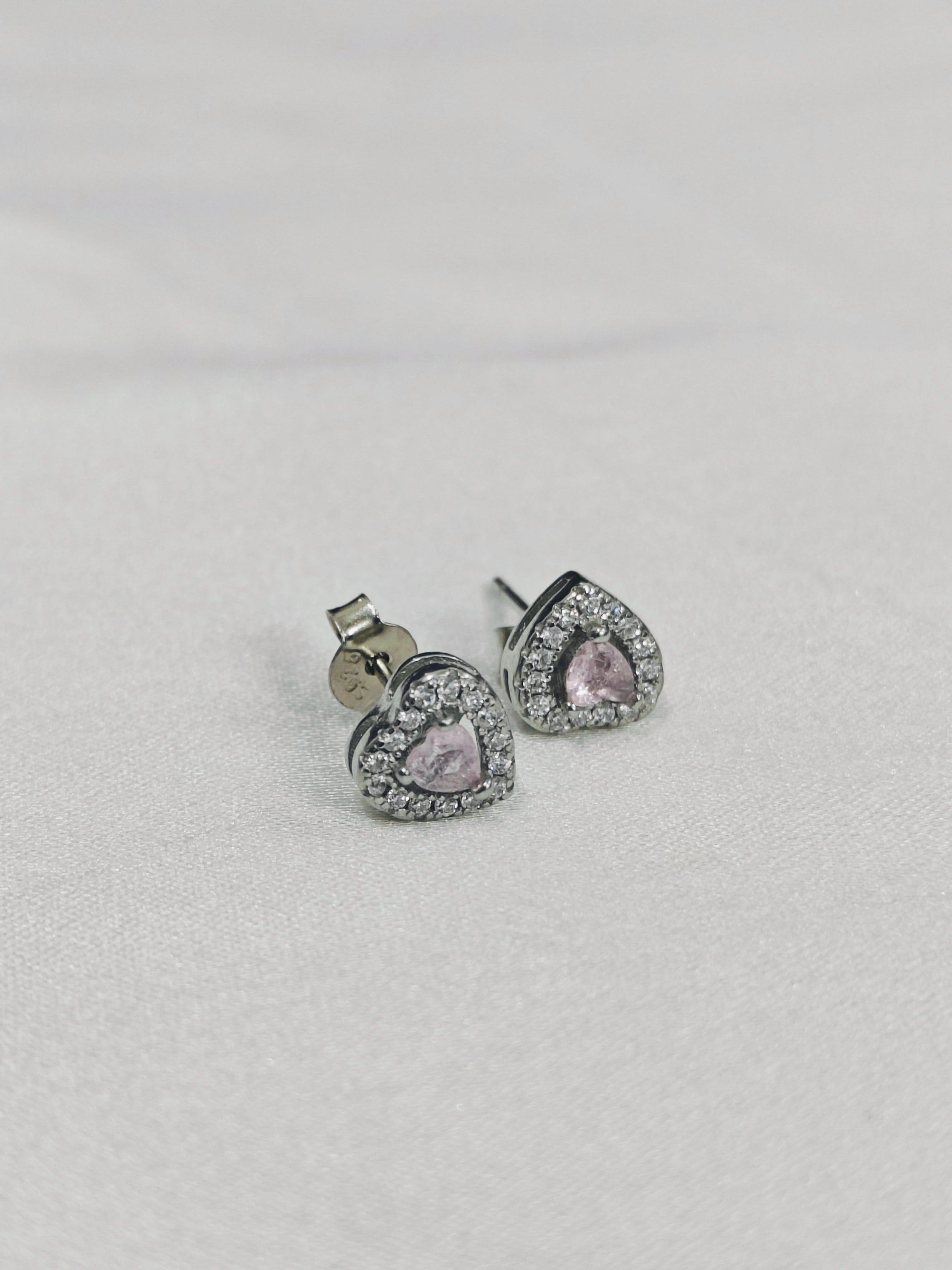 Heart-shaped earrings with pink gemstones on a light gray background